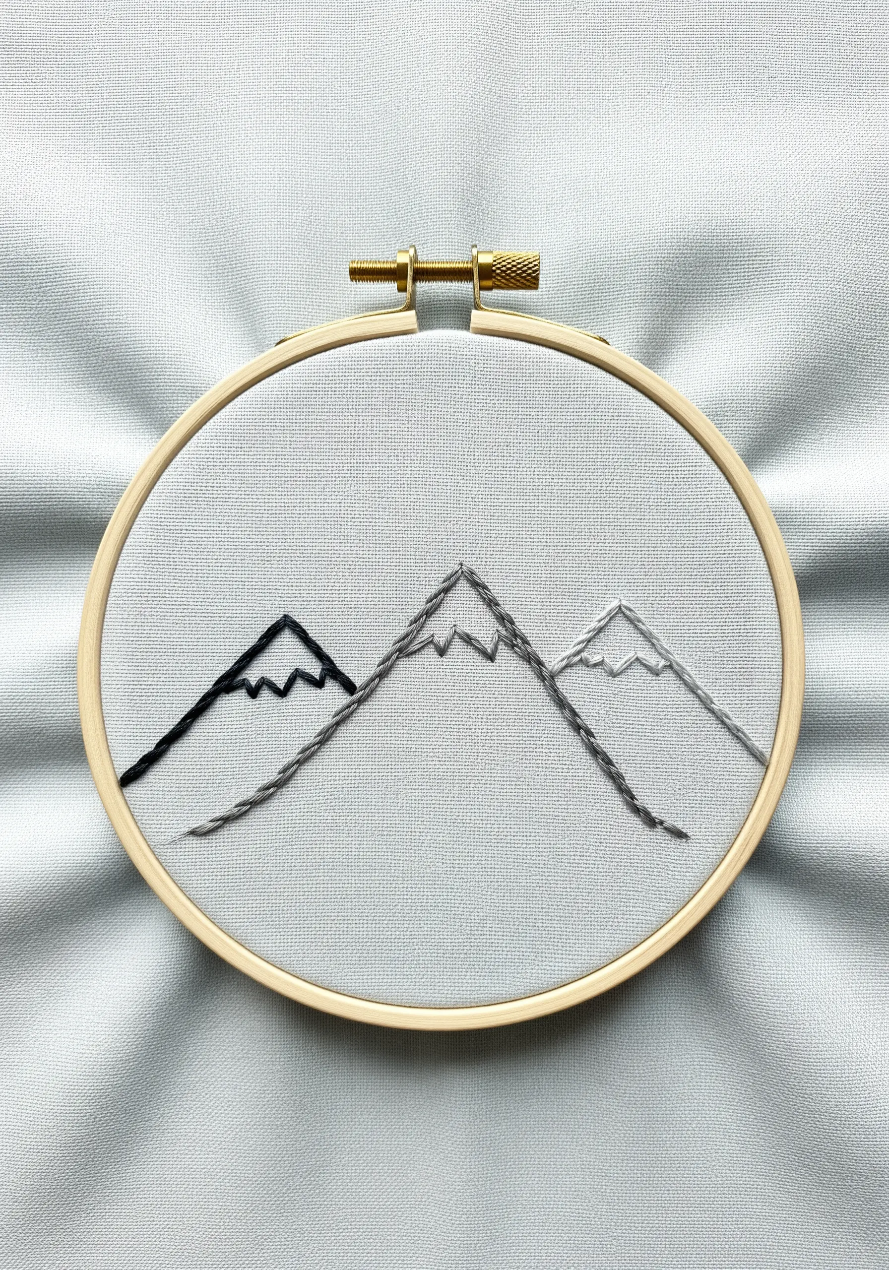 A minimalist embroidery of three mountain peaks in black, grey, and light grey thread.