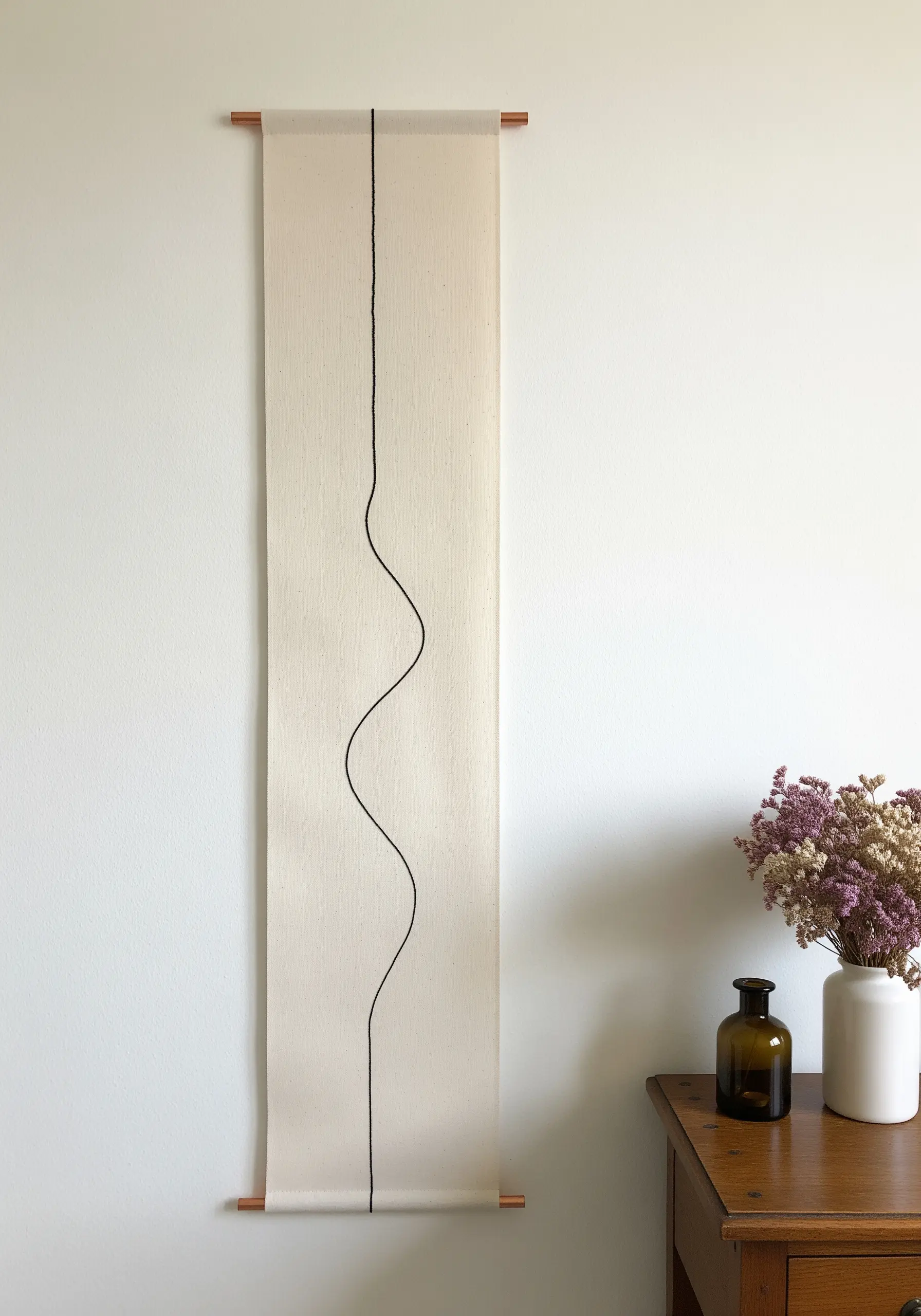 A long, narrow fabric wall hanging with a single, minimalist black wavy line embroidered down the center.