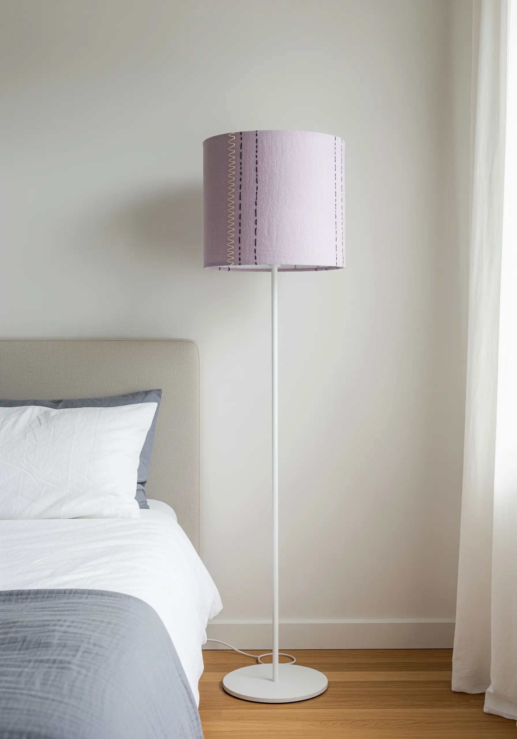 A lavender floor lamp with a simple, modern design, featuring vertical hand-stitched lines.