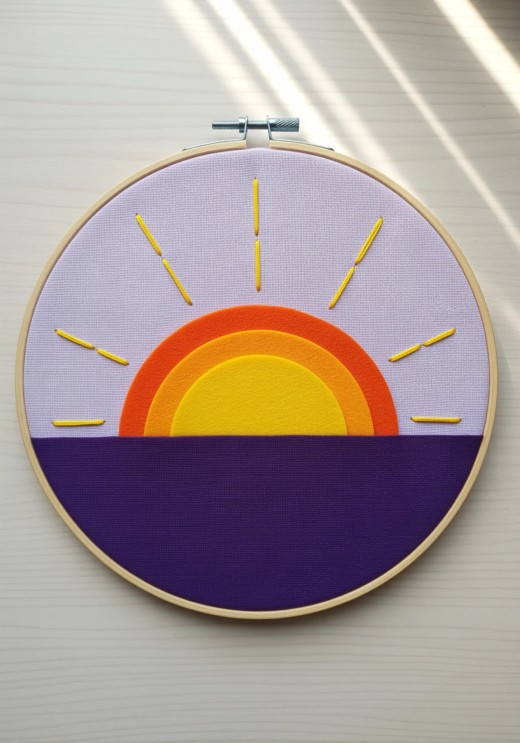 A minimalist fabric collage sunset with layered felt and yellow straight stitches for sun rays.