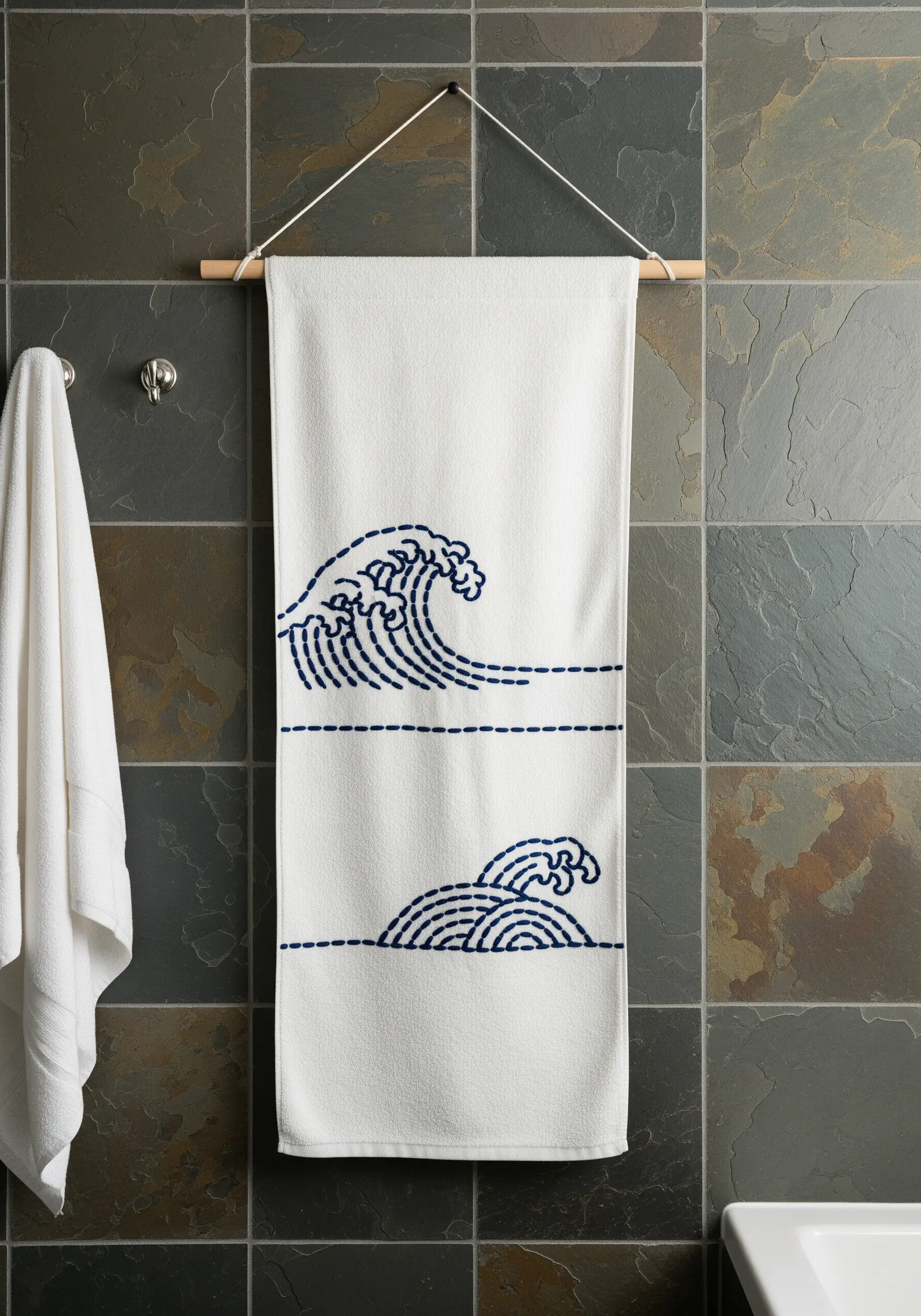 A white towel with two minimalist, Japanese-style wave motifs embroidered in navy blue thread.