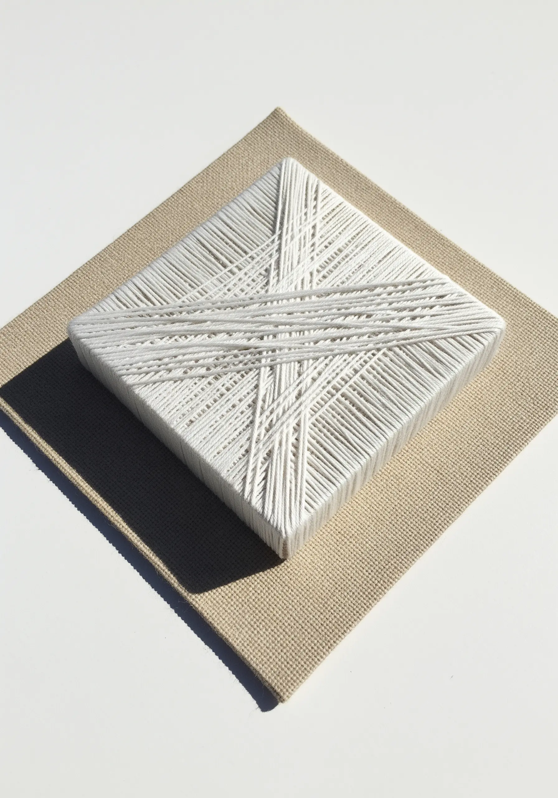 White thread wrapped in a geometric, layered pattern over a square white canvas block.