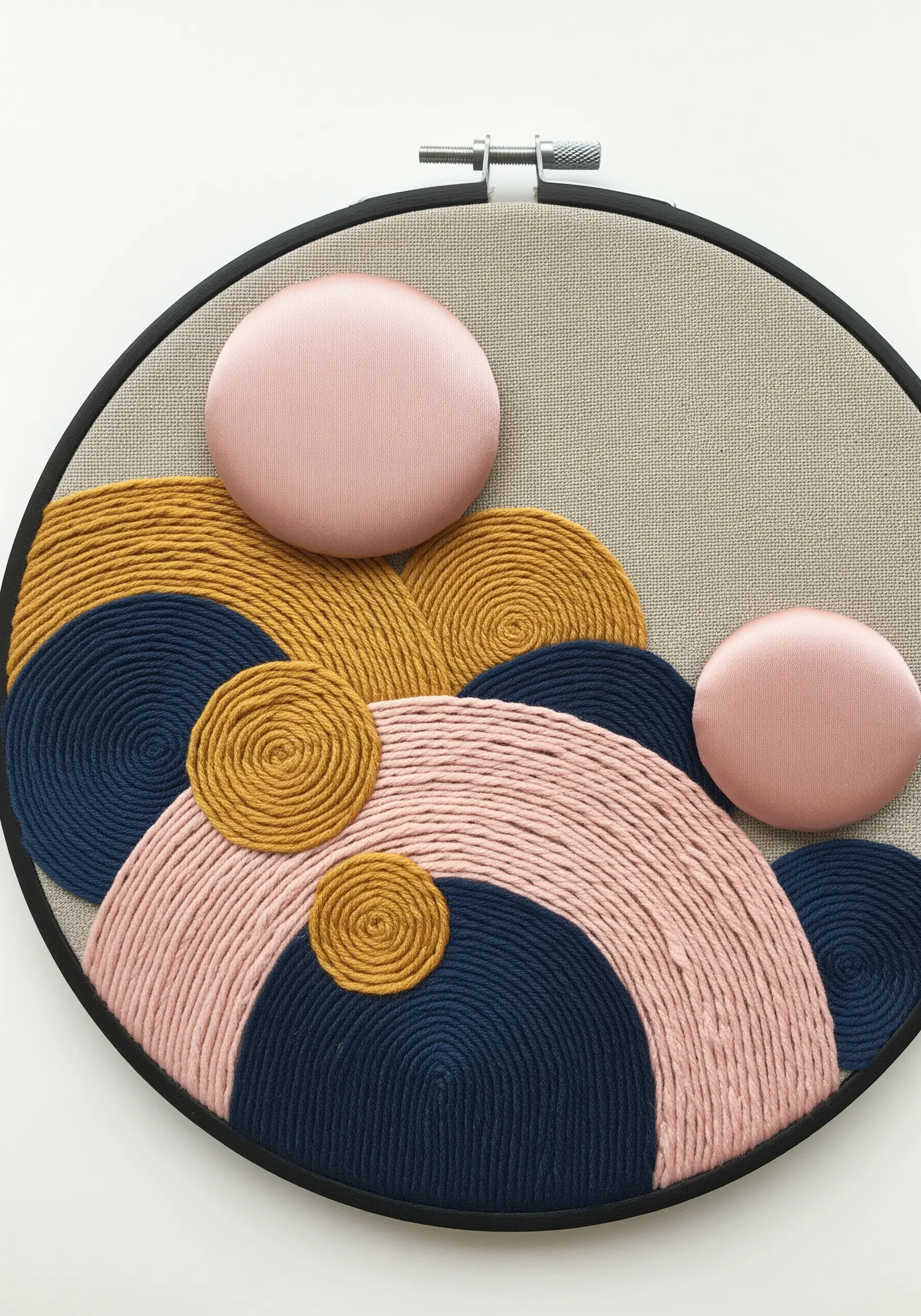 Abstract hoop art combining pink padded satin stitch circles with couched yarn in navy and gold.