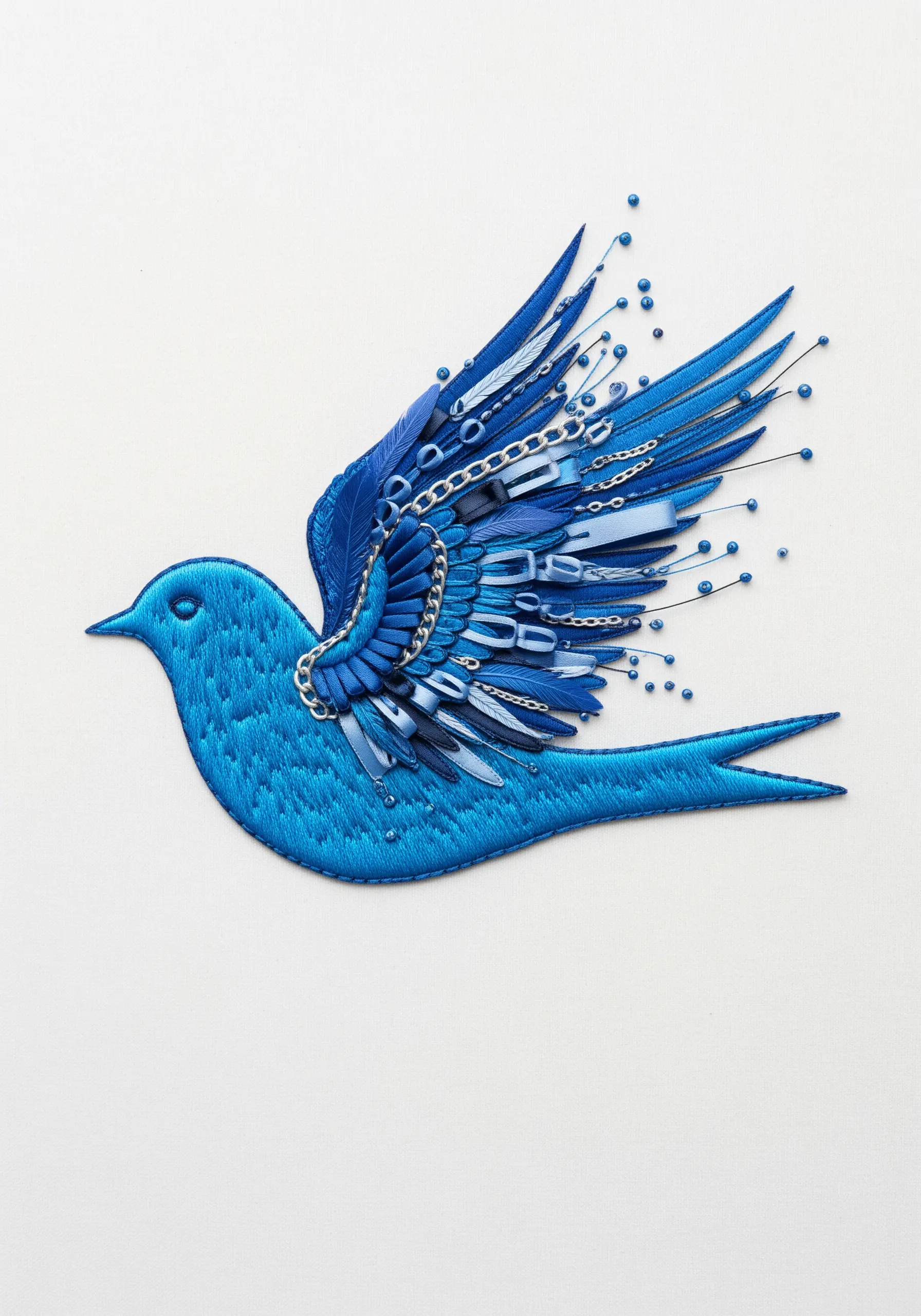 A satin-stitched blue bird with wings made of layered ribbon, beads, and chains.