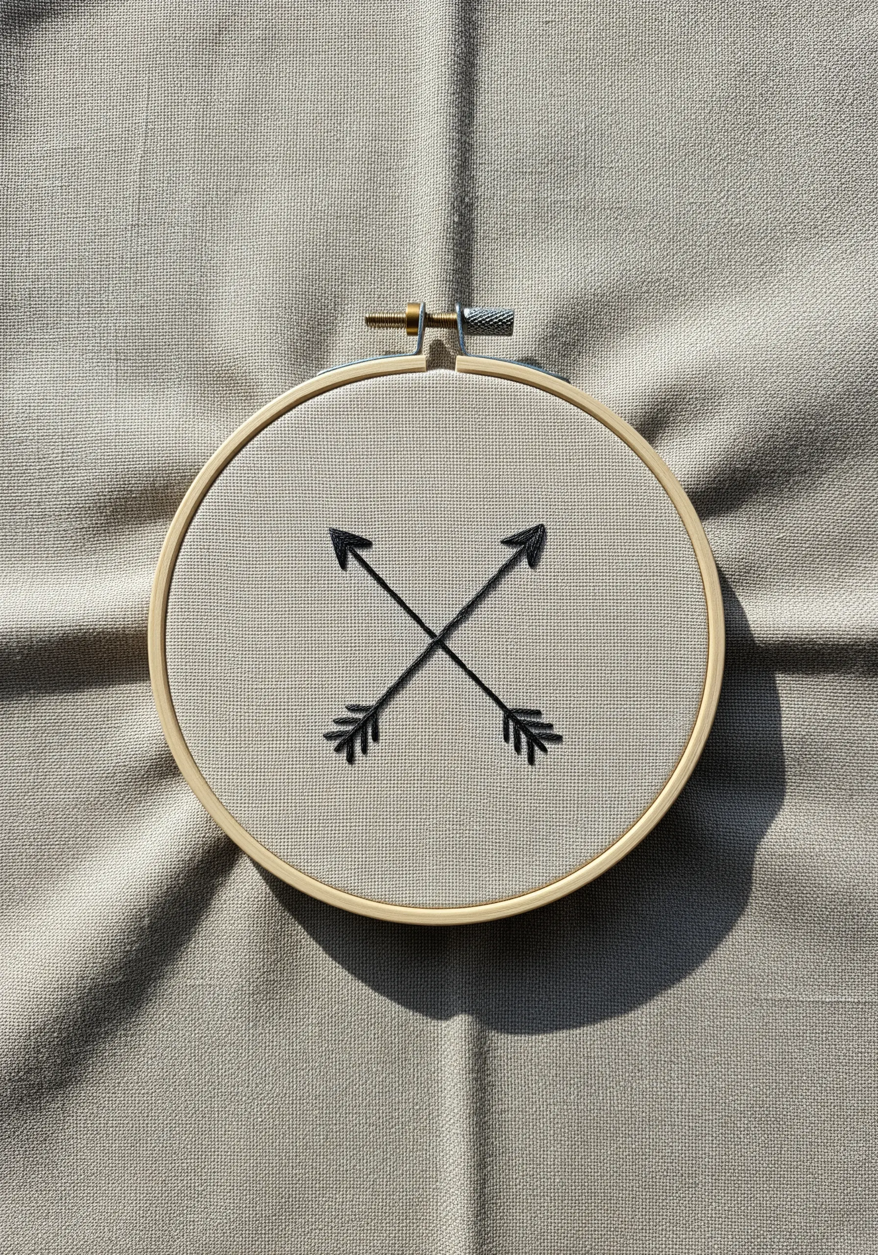 Two minimalist black crossed arrows embroidered on neutral linen-like fabric.