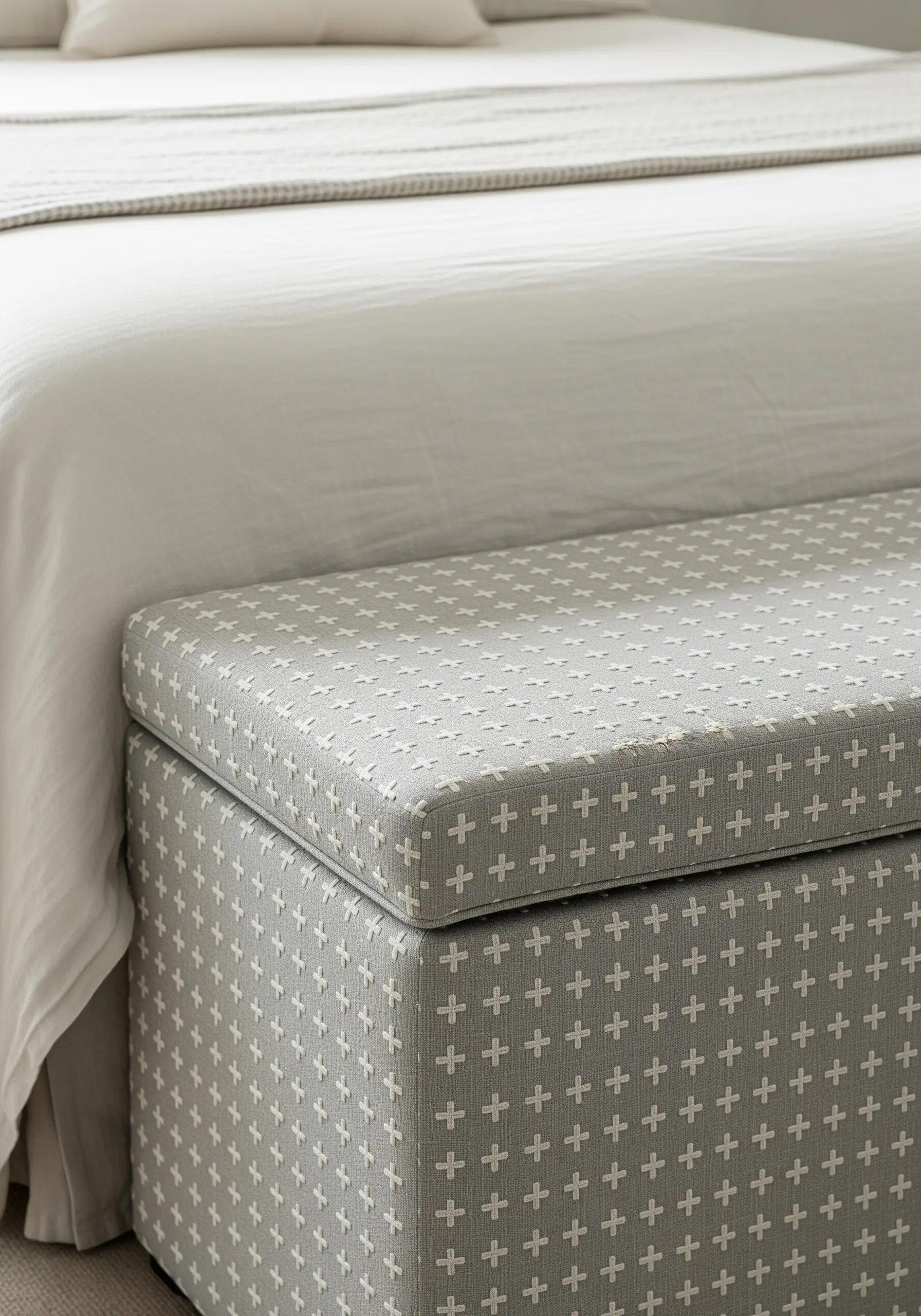A grid pattern of white plus-sign stitches on a grey upholstered bench.