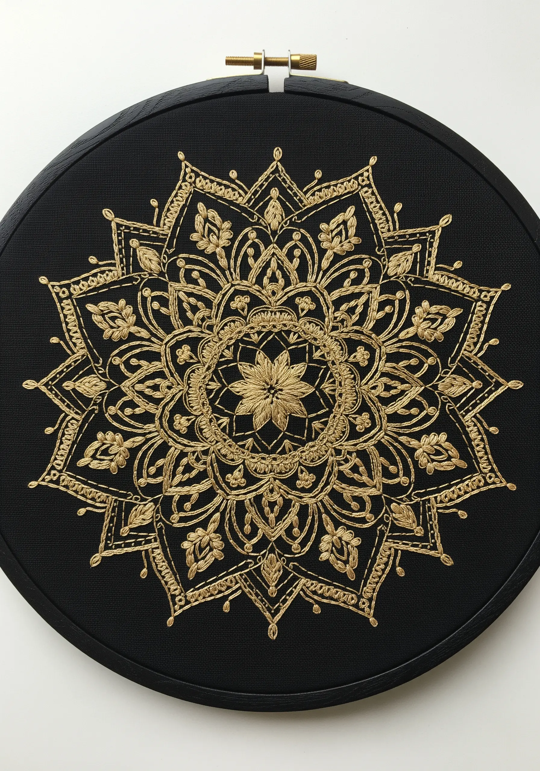 An intricate gold mandala embroidered on black fabric, displayed in a black hoop.
