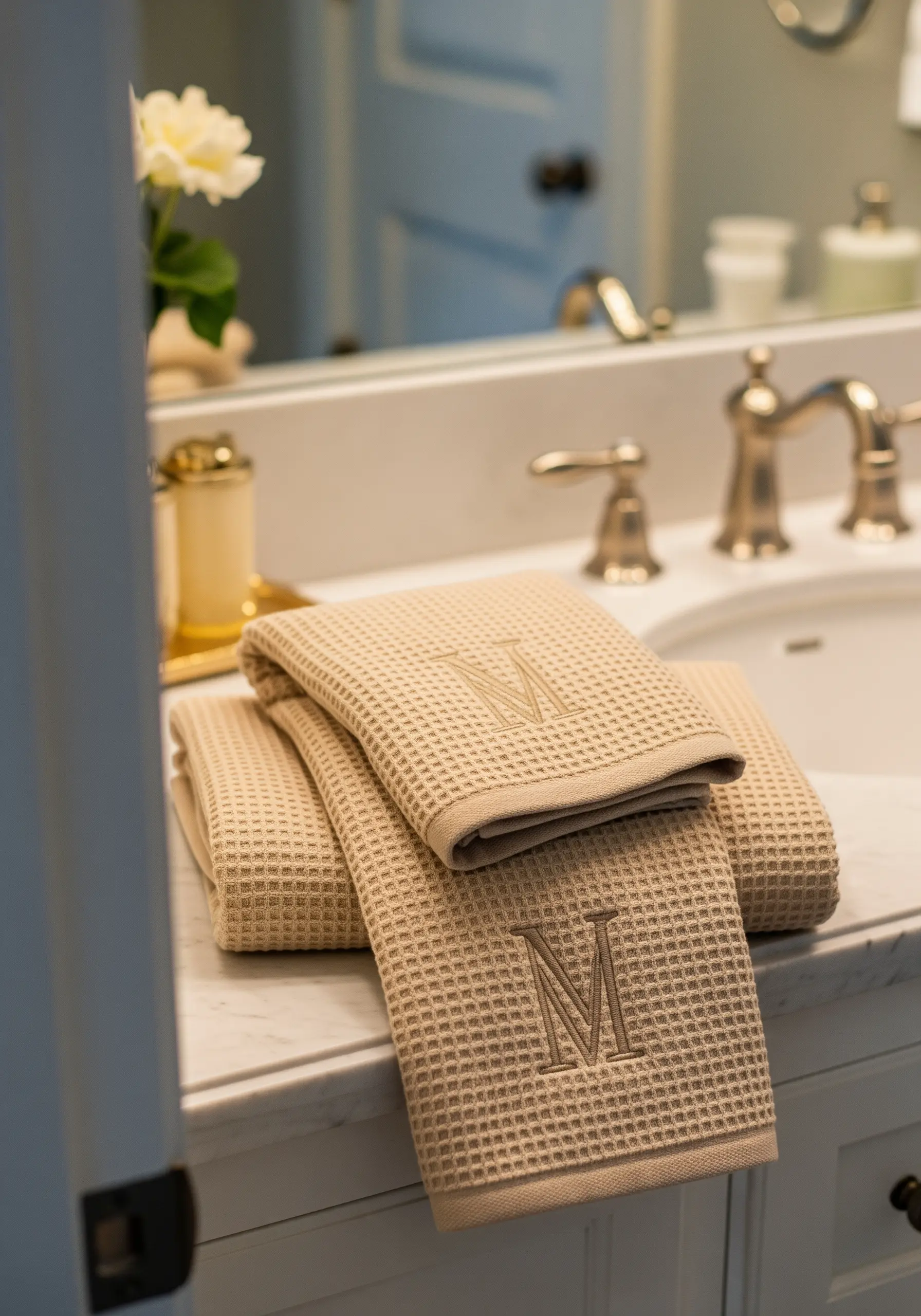 A tone-on-tone satin stitch monogram 'M' embroidered on a beige waffle-weave towel.