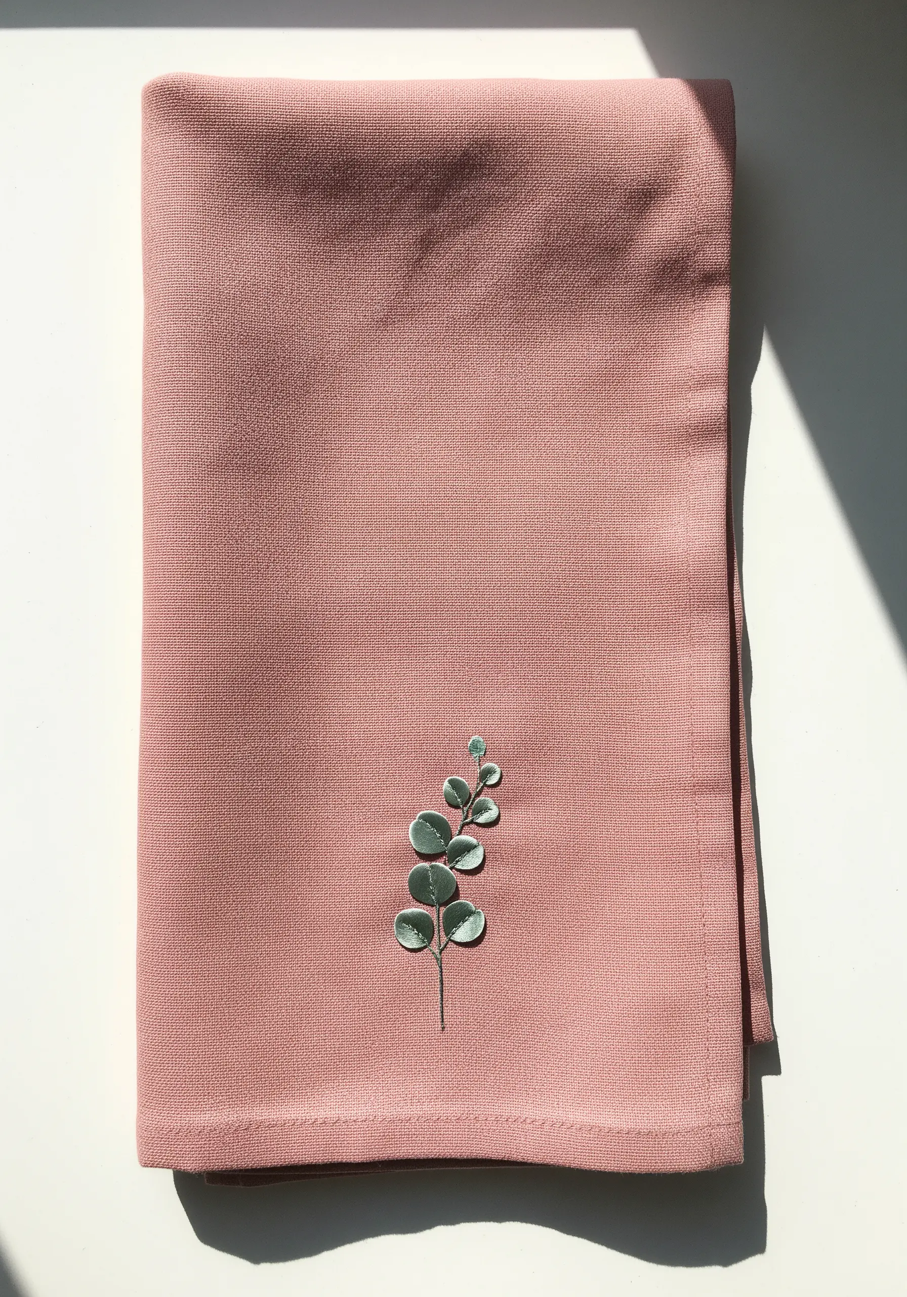A sprig of eucalyptus with satin-stitched leaves on a dusty rose linen napkin.