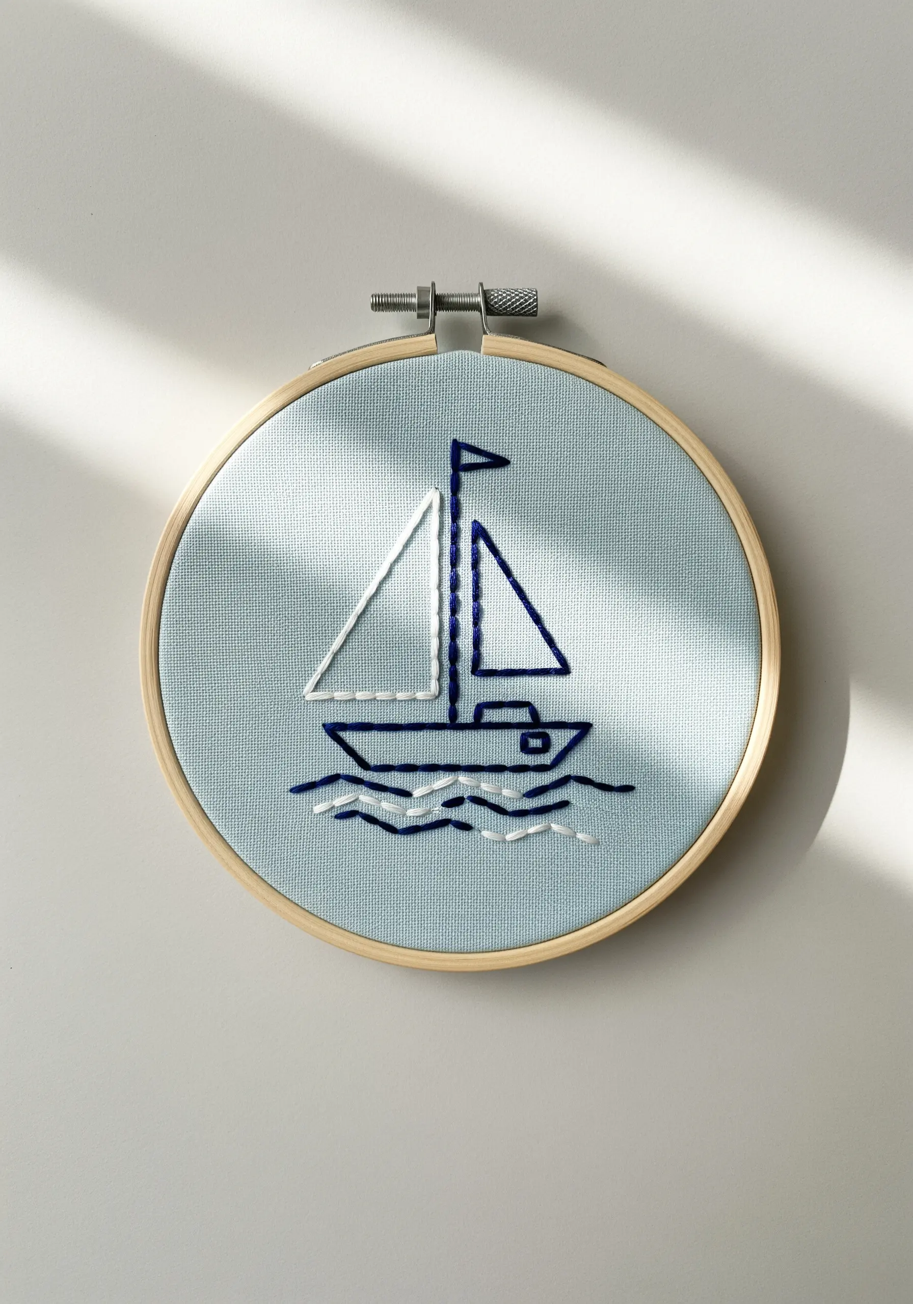 Minimalist line art sailboat using whipped backstitch on light blue fabric.