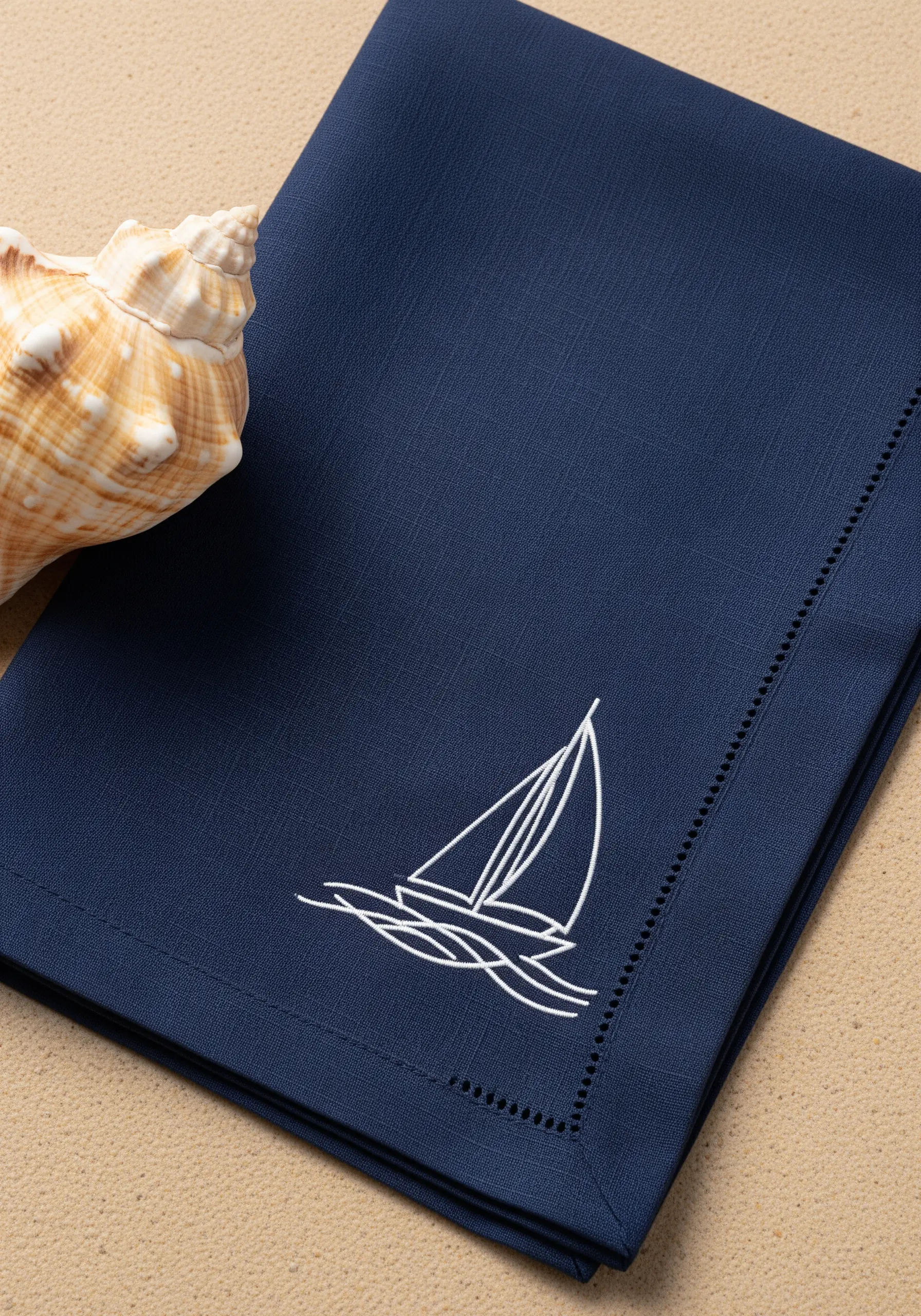 White line art sailboat and waves embroidered on a dark navy blue napkin.