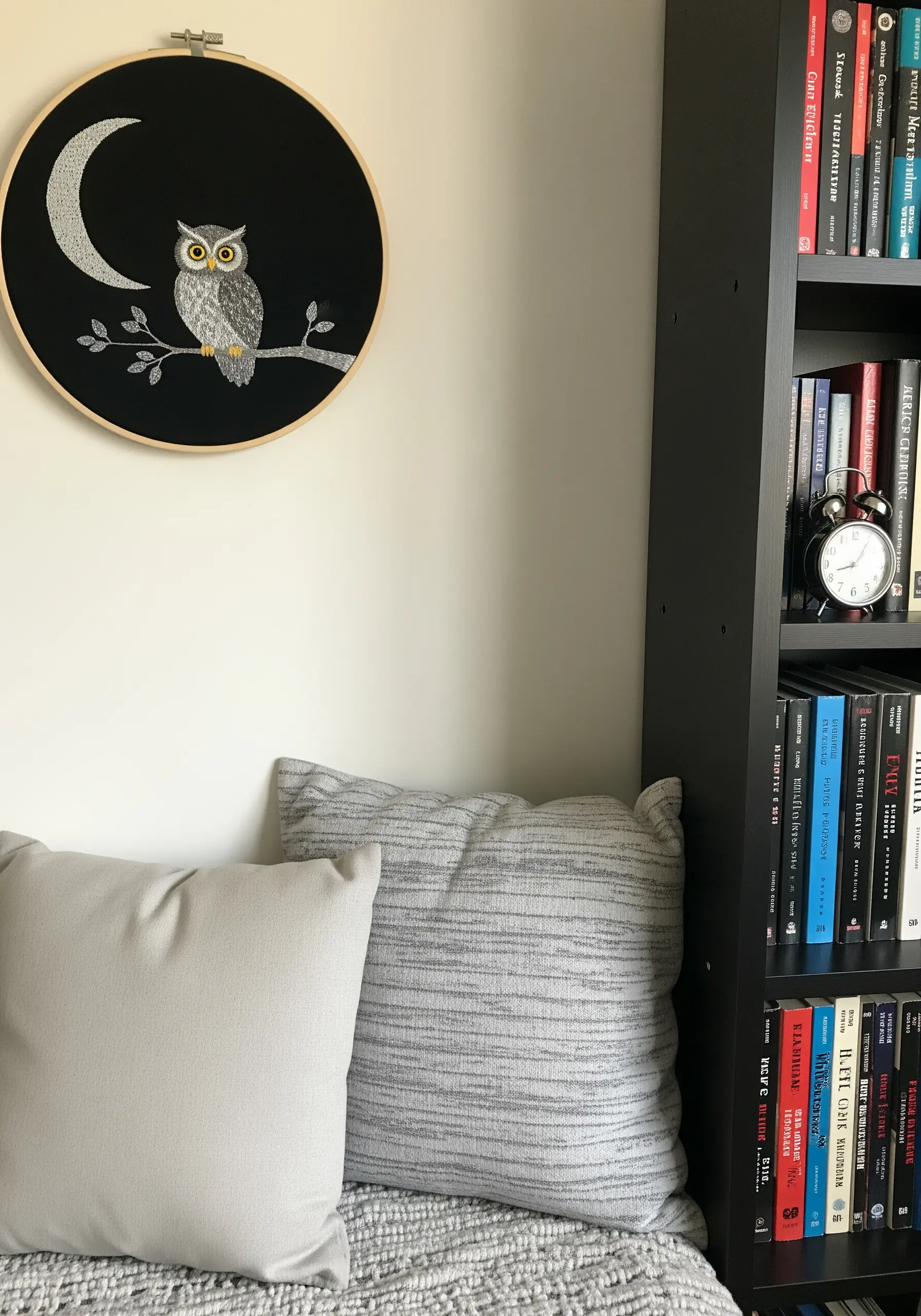 An embroidery hoop with an owl on a branch against a crescent moon, stitched on black fabric.