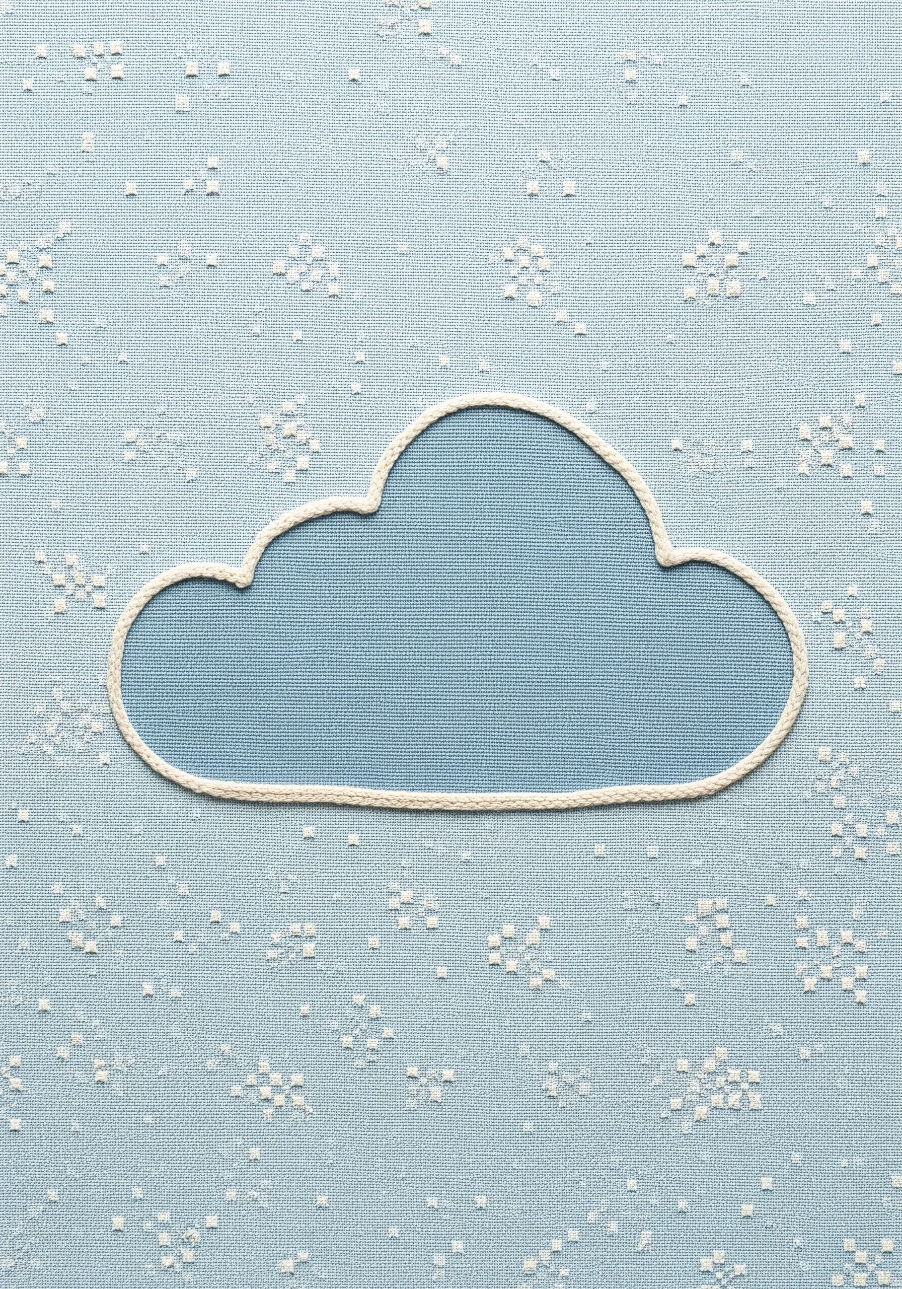 A blue fabric cloud shape appliquéd and outlined with white stitching on patterned blue fabric.