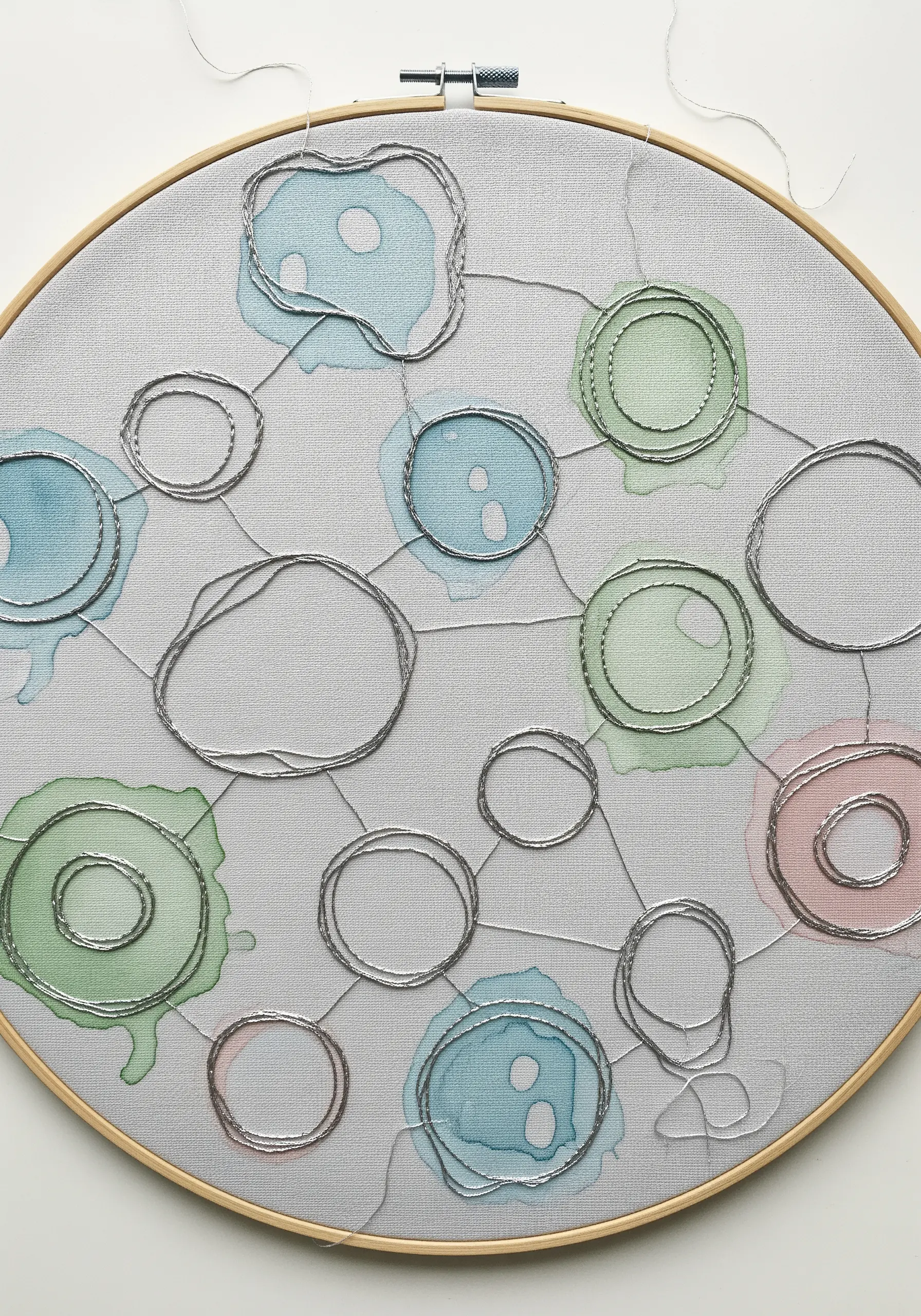 Watercolor splotches on fabric outlined with organically shaped silver metallic stitches.