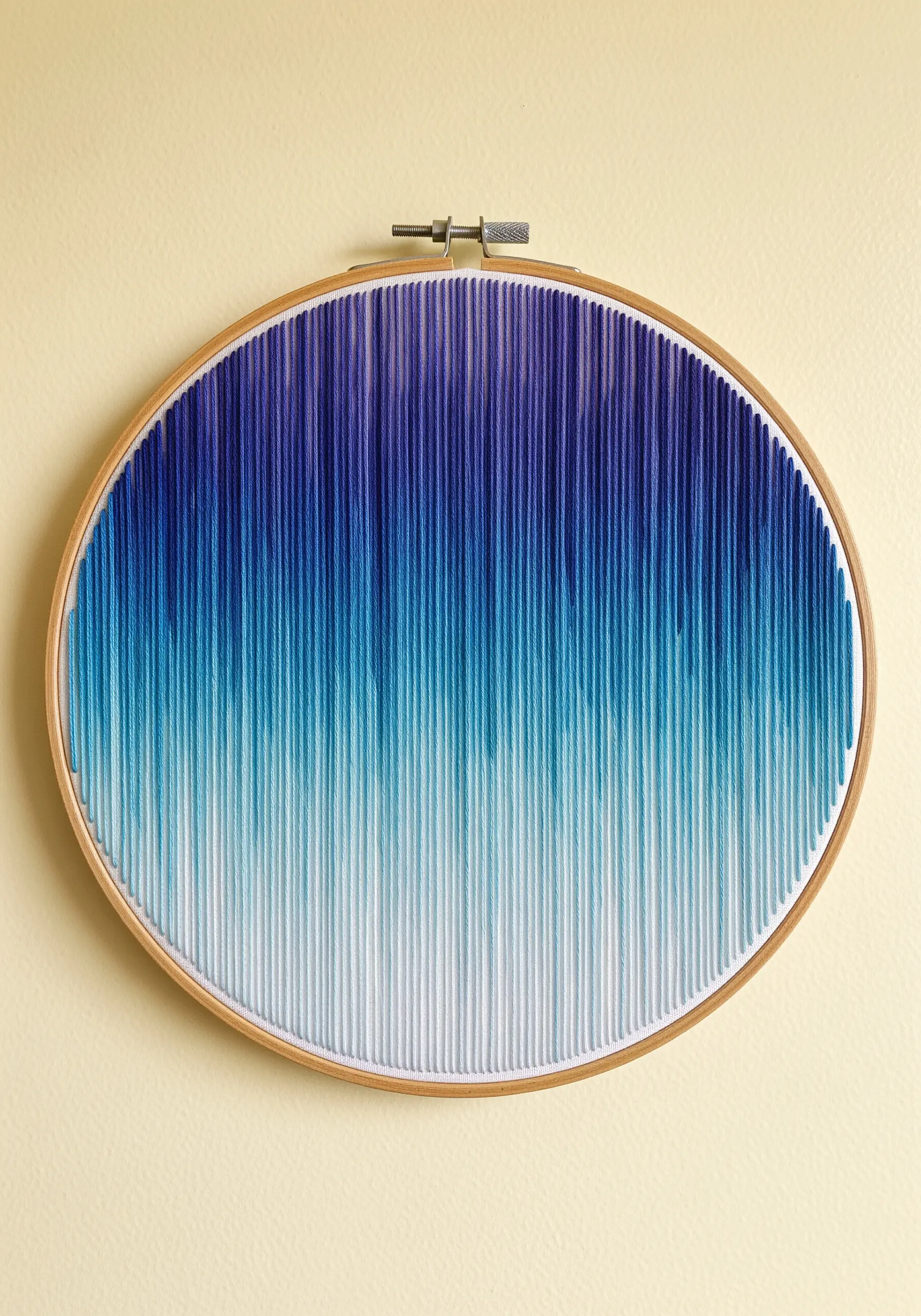 An oval hoop filled with vertical stitches creating a smooth gradient from dark blue to white.