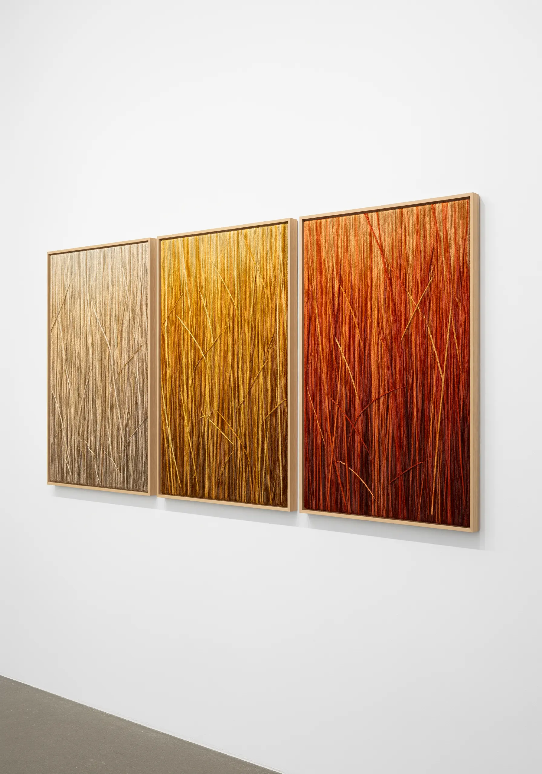 A triptych of framed art showing dense, vertical embroidery in gradients of beige, yellow, and orange.