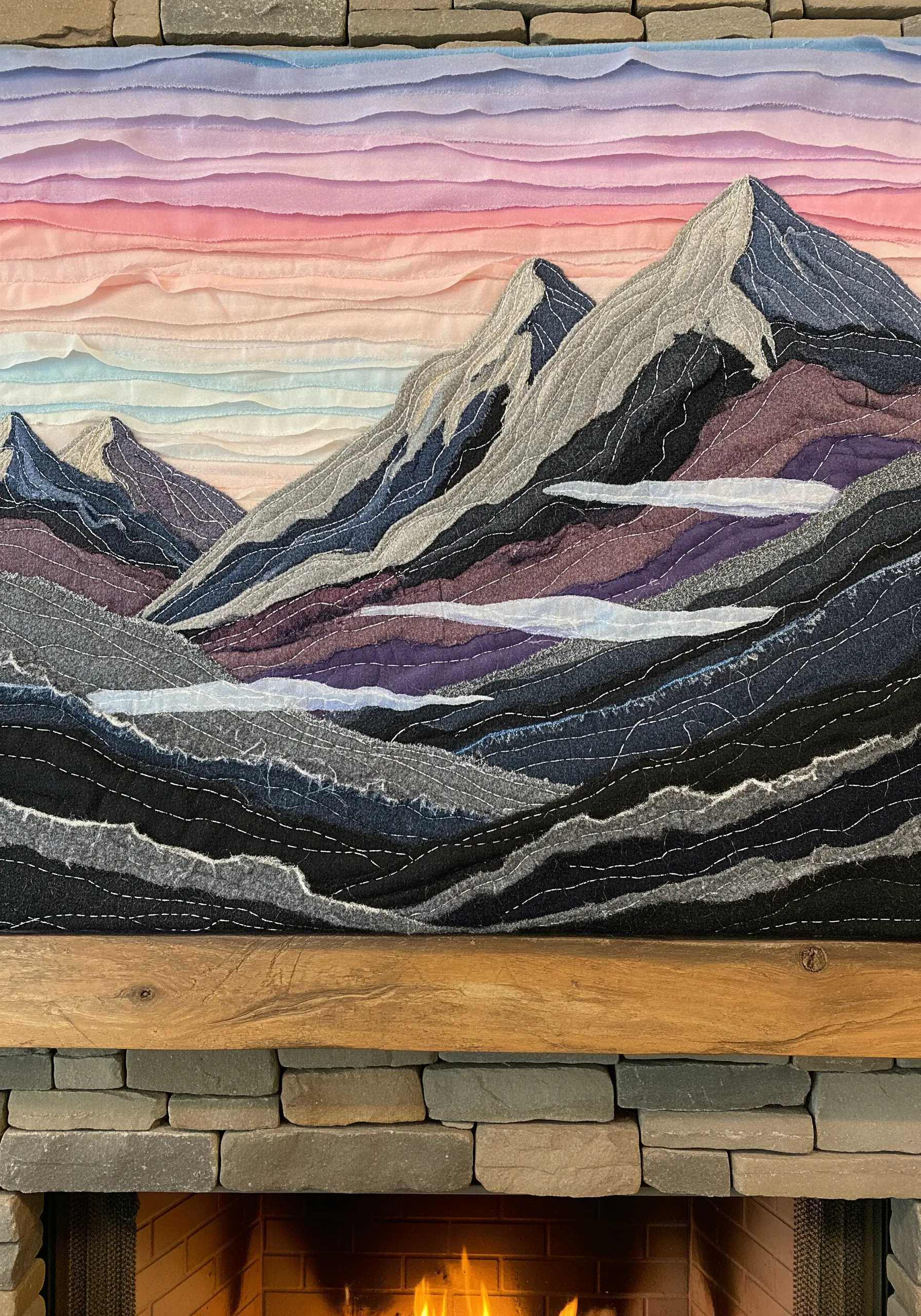 A large textile wall hanging of a mountain range at sunset, made from torn fabric strips