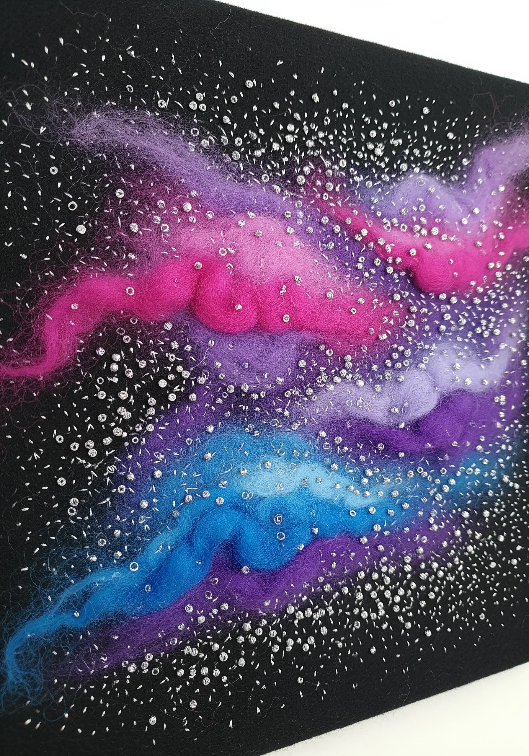 Mixed-media embroidery of a colorful galaxy using wool roving and beads on black fabric.