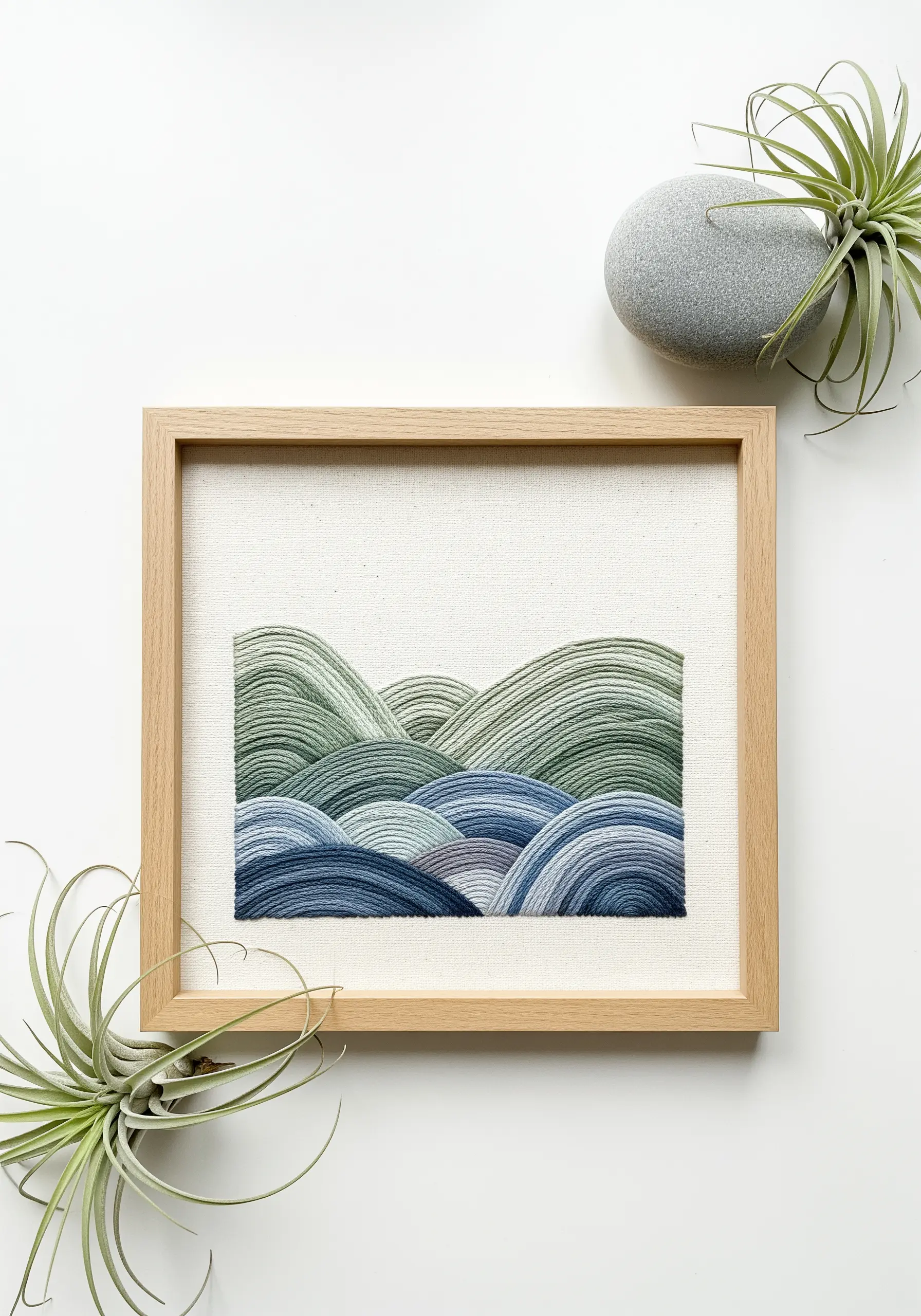 Framed embroidery of rolling hills in shades of green and blue, creating a layered landscape.