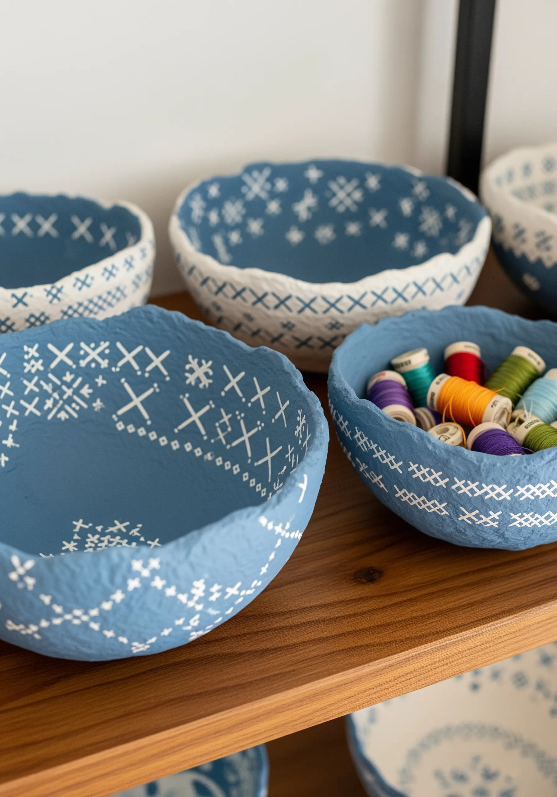 Blue and white papier-mâché bowls painted with patterns that mimic cross-stitch designs.
