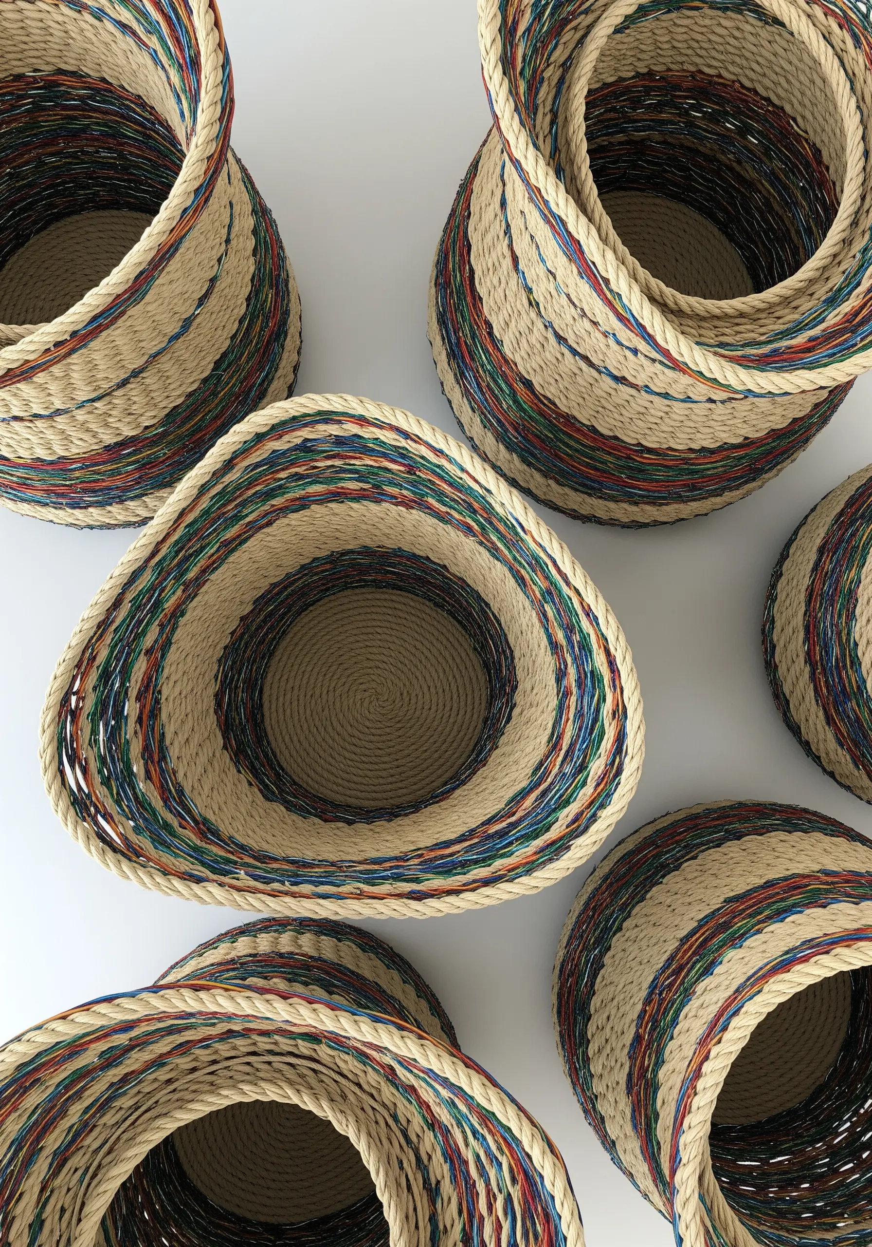 Overhead view of several coiled rope baskets with colorful threads wrapped around the rope.
