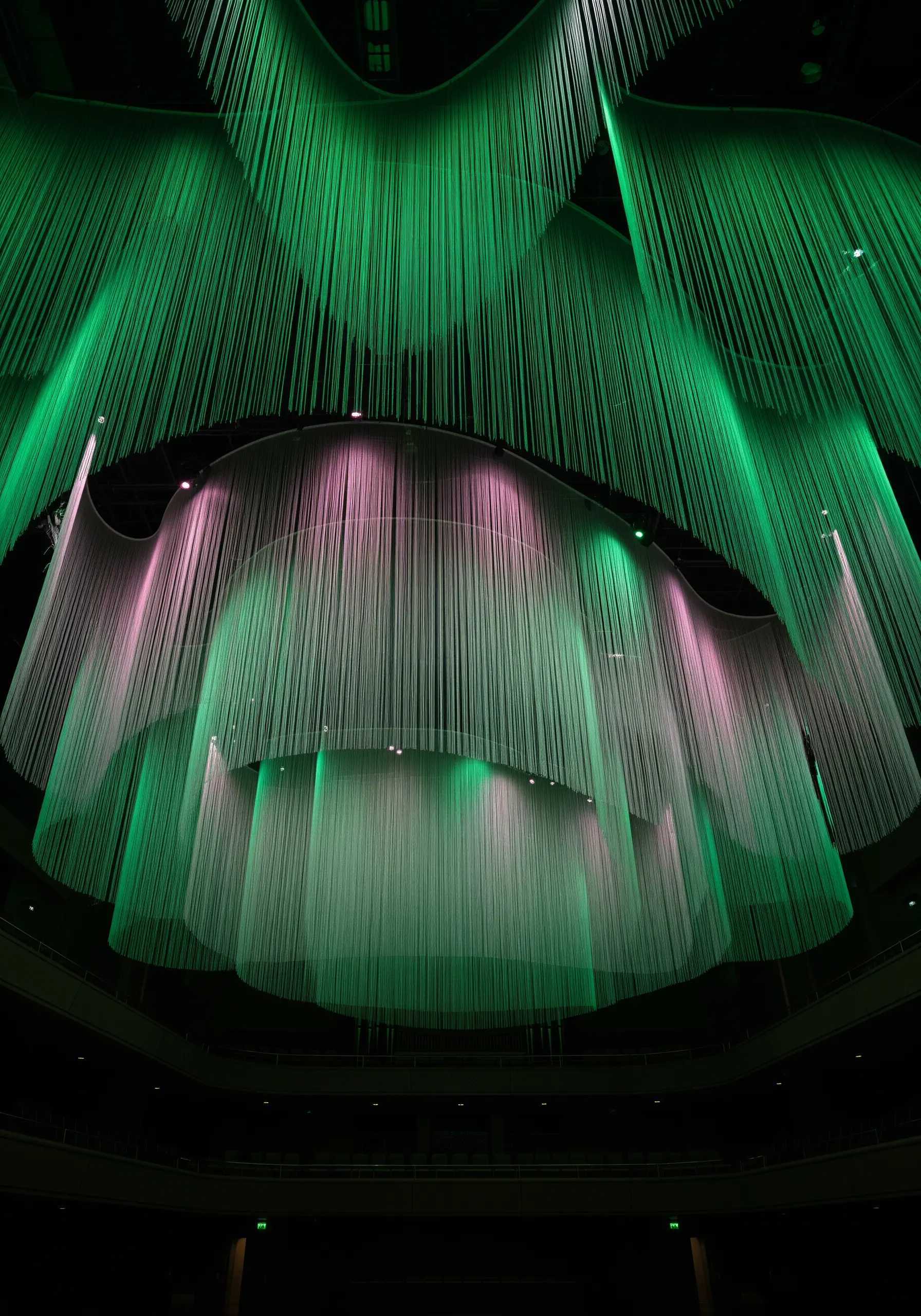 An ethereal ceiling installation of draped, translucent fabric illuminated with green and pink light.