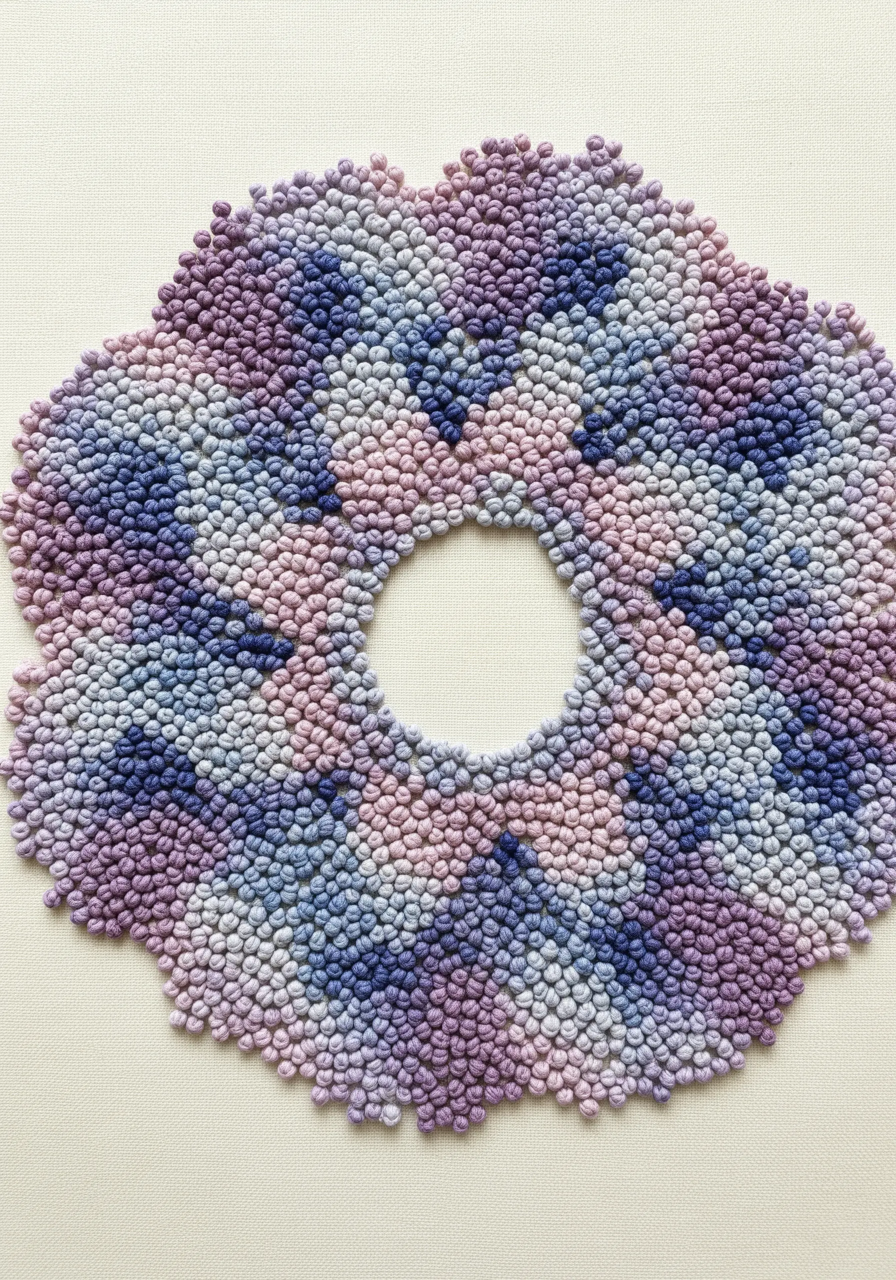 A floral-shaped mandala filled entirely with French knots in shades of purple and blue.