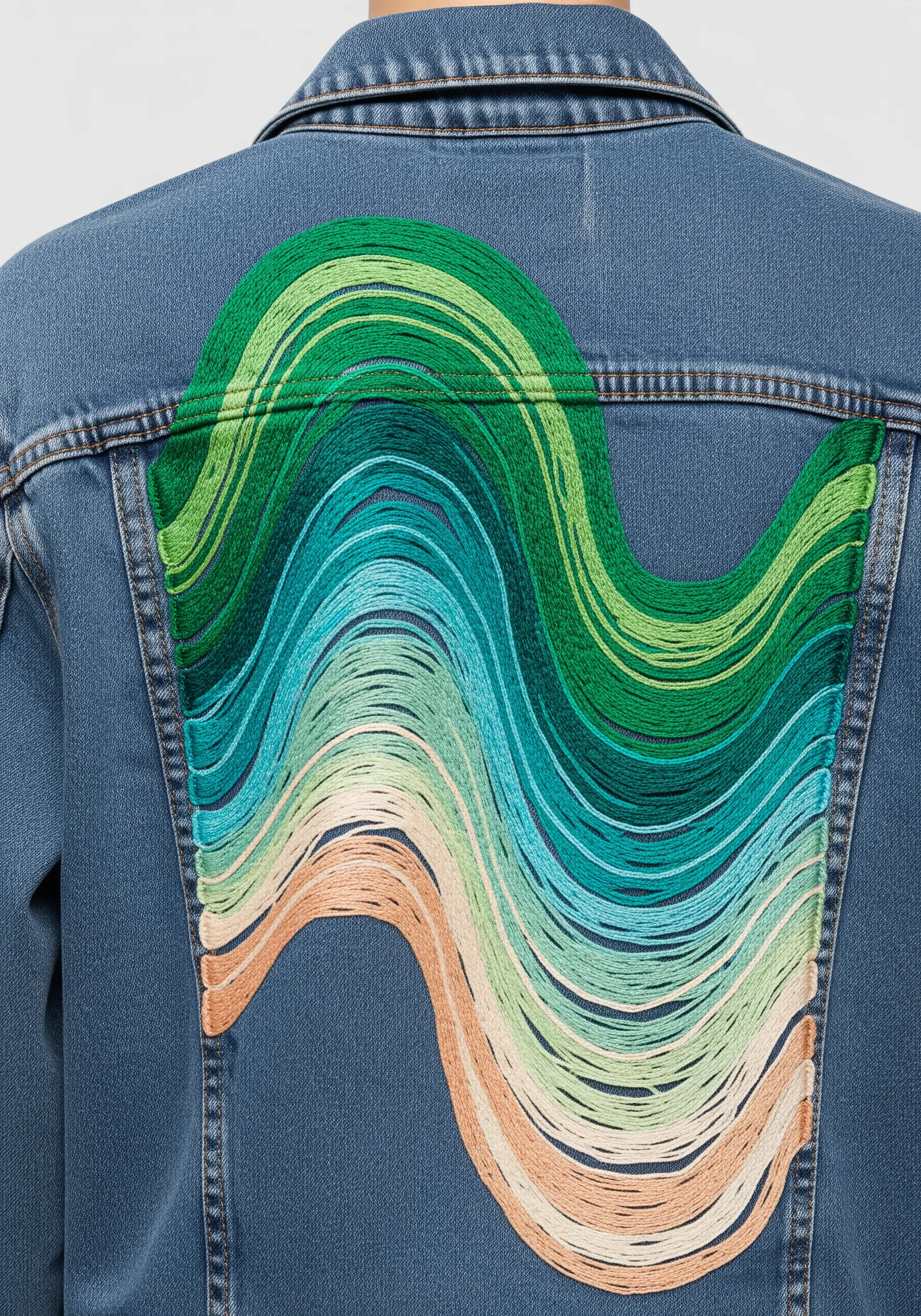 A large, wavy abstract design on a denim jacket made with long, flowing threads in a green gradient.