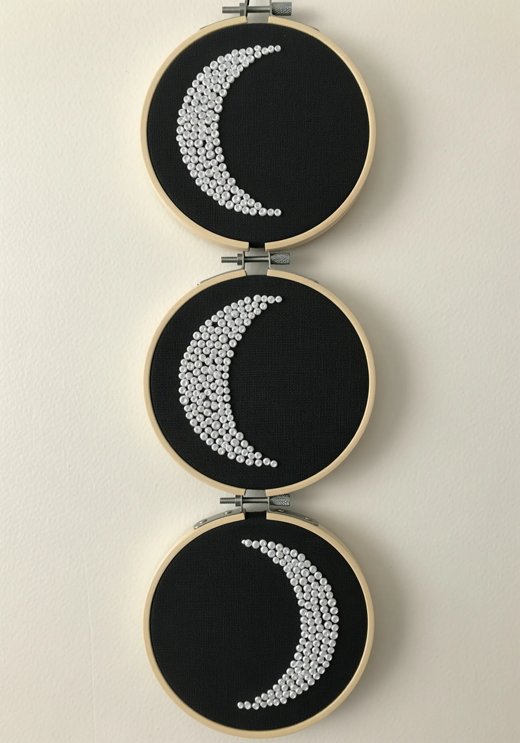 Three embroidery hoops with crescent moons filled with white French knots on black fabric.