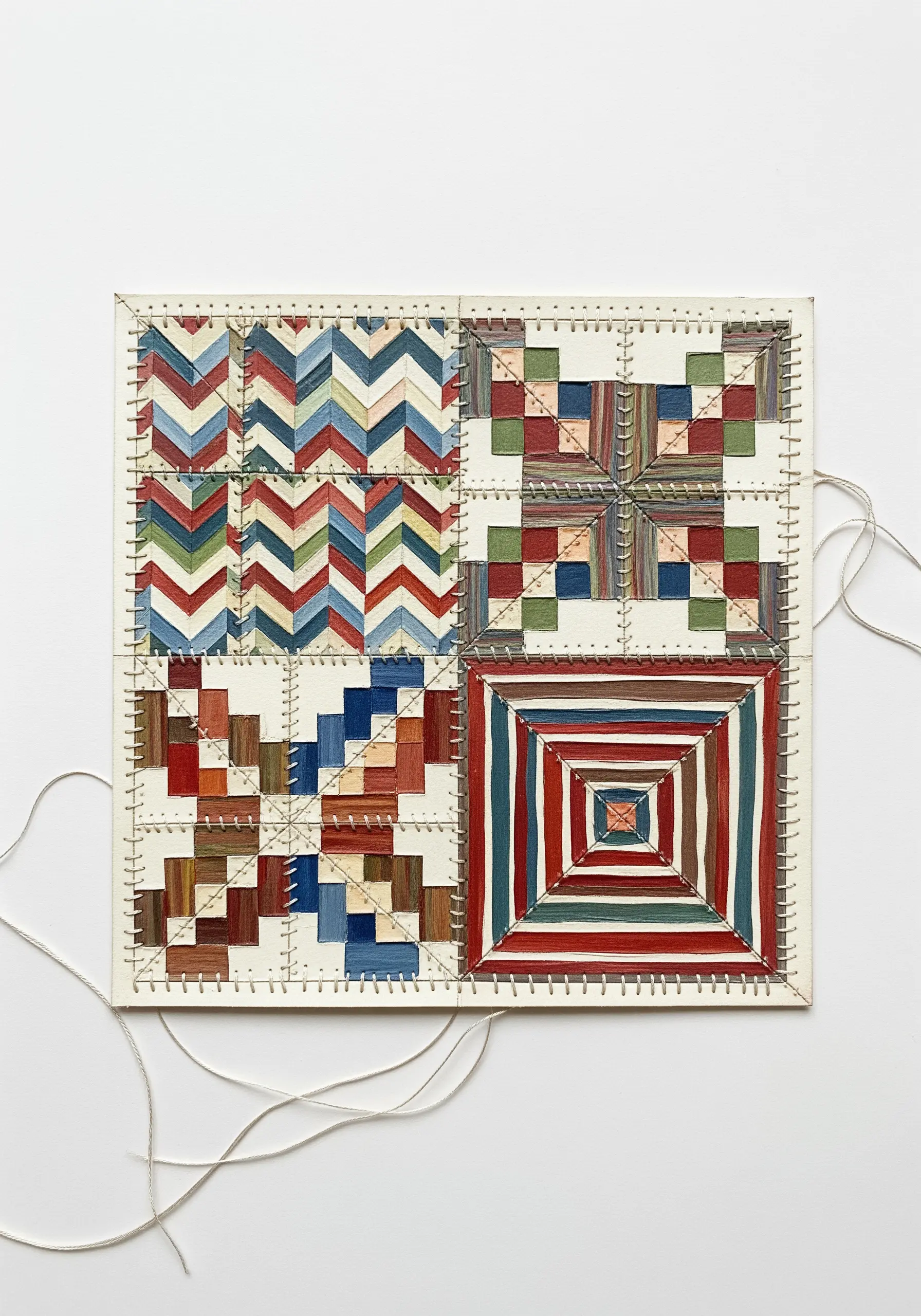 Four painted quilt block patterns on paper with decorative hand stitching.