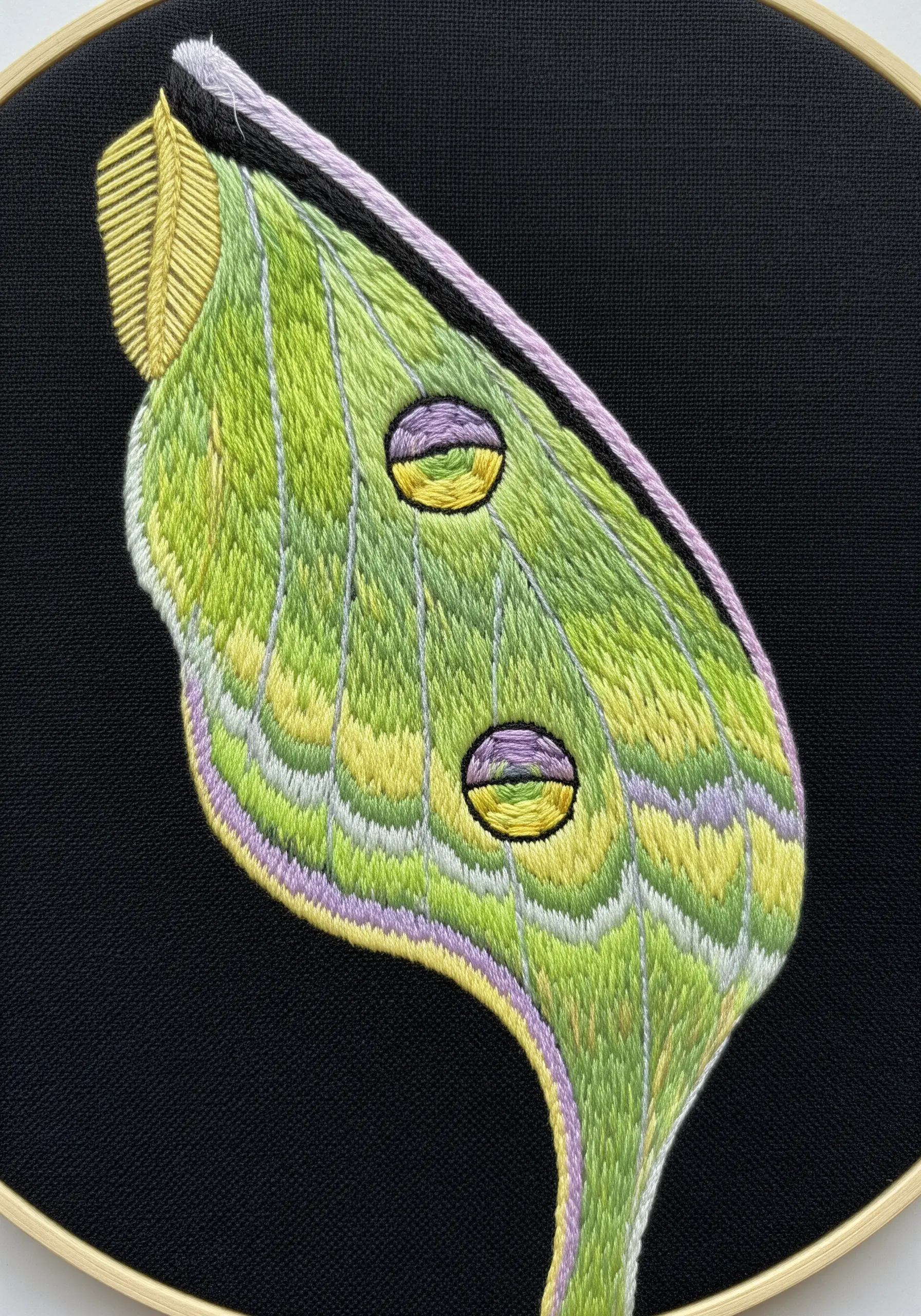 A detailed close-up of an embroidered Luna Moth wing, showing soft color blending.