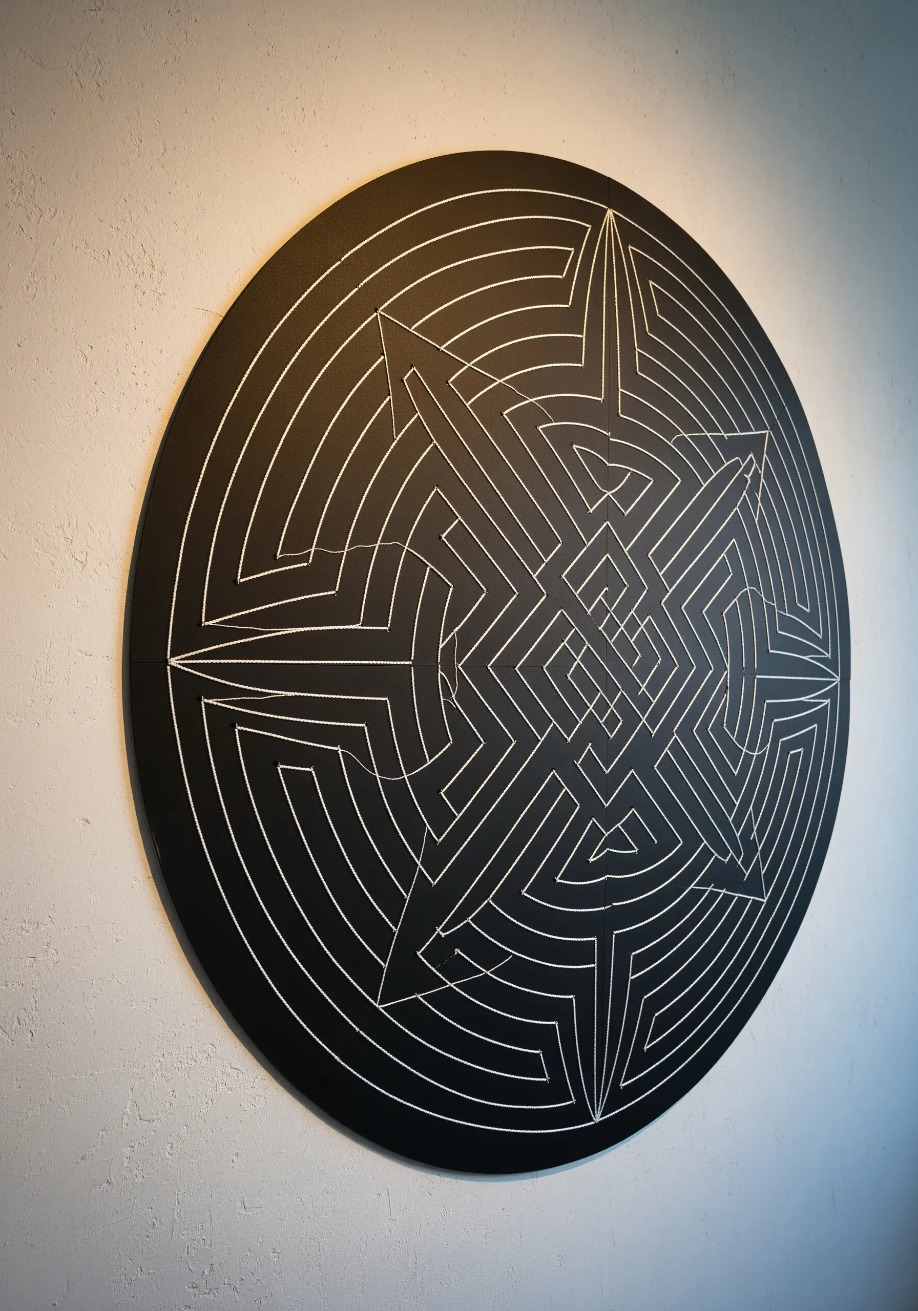A circular black paper-cut labyrinth with a single white thread tracing a path through it.
