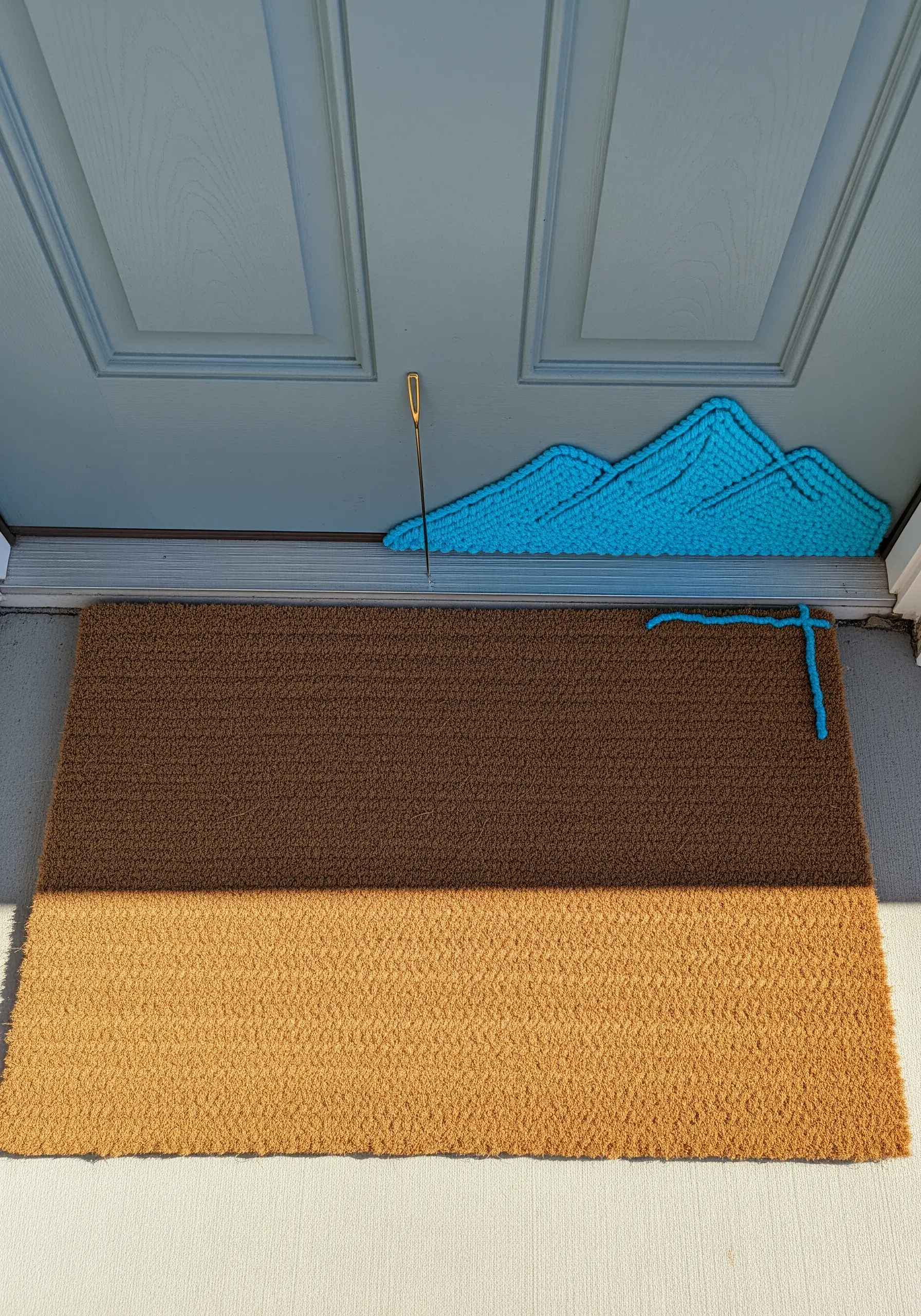 Bright blue yarn stitched in a mountain shape onto the corner of a coir doormat.