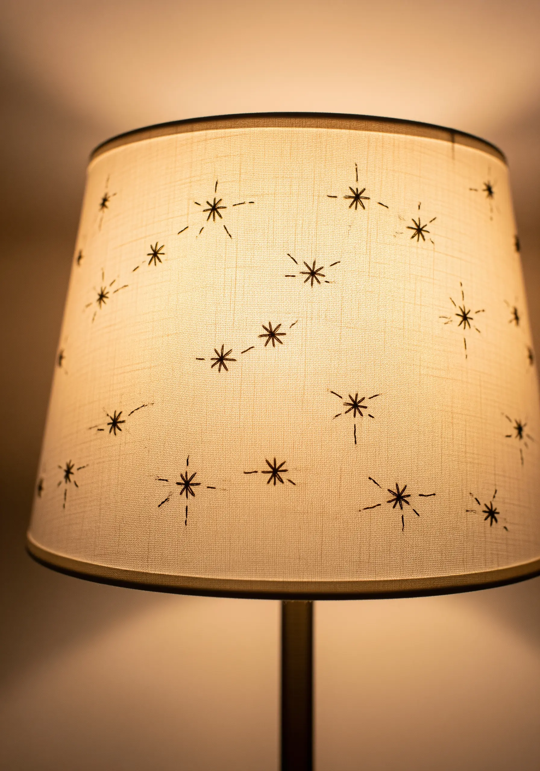 A cream-colored fabric lampshade embroidered with a scattered pattern of dark, minimalist starbursts.