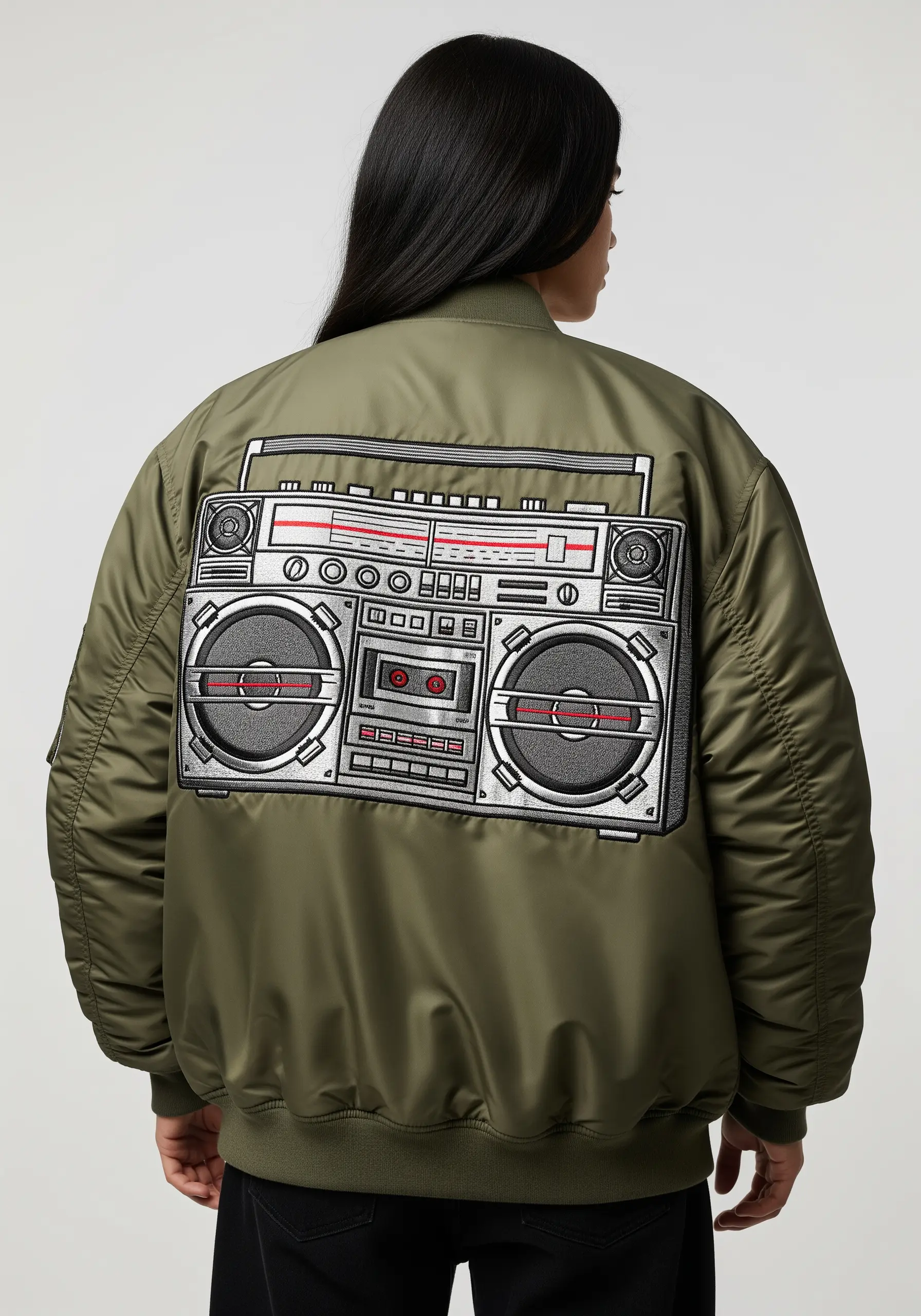 Large, detailed embroidery of a retro boombox on the back of an olive bomber jacket.