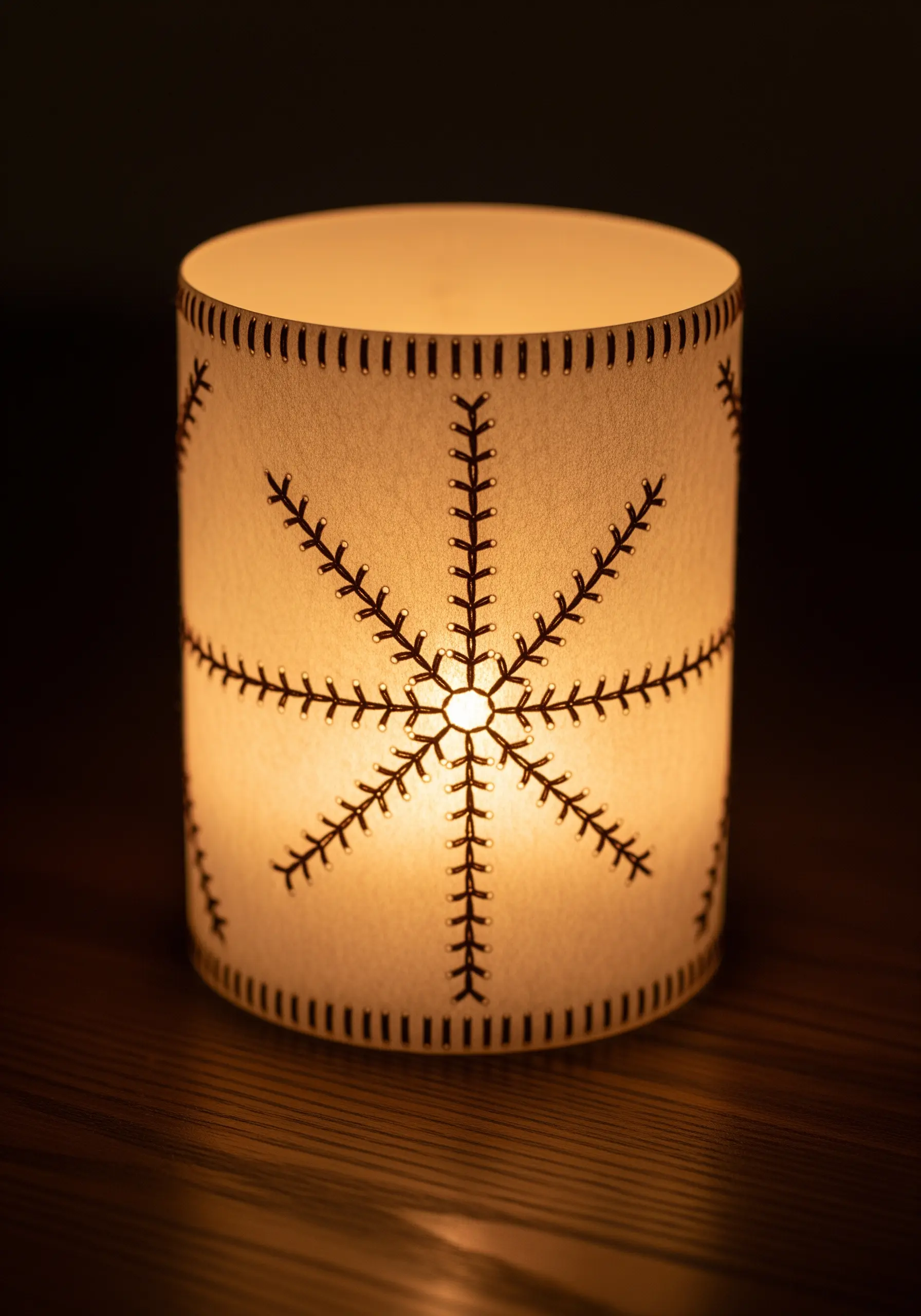 A cylindrical paper lantern illuminated from within, showcasing a stitched snowflake design.