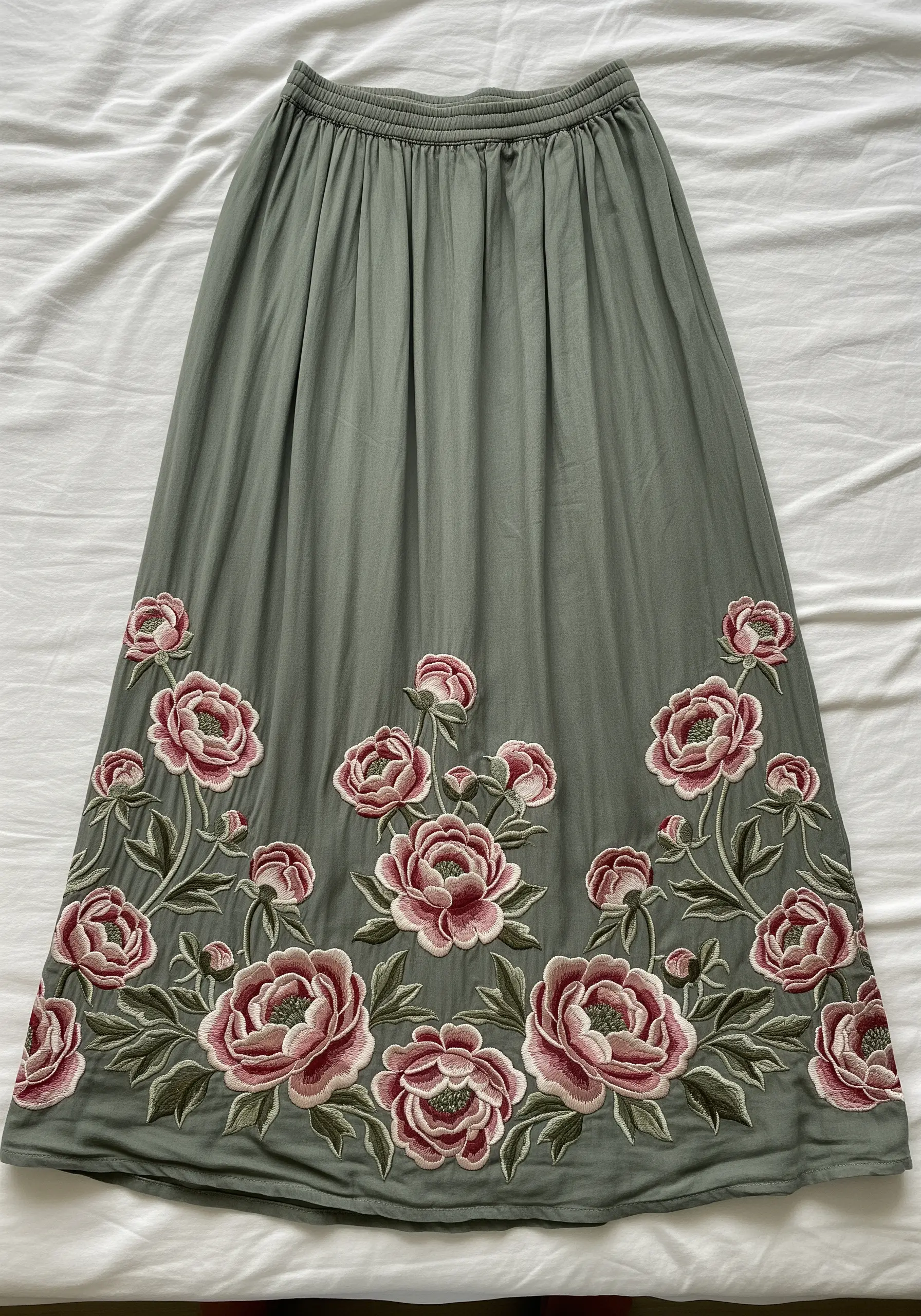 A repeating pattern of pink peonies and buds embroidered along the hem of a long green skirt.