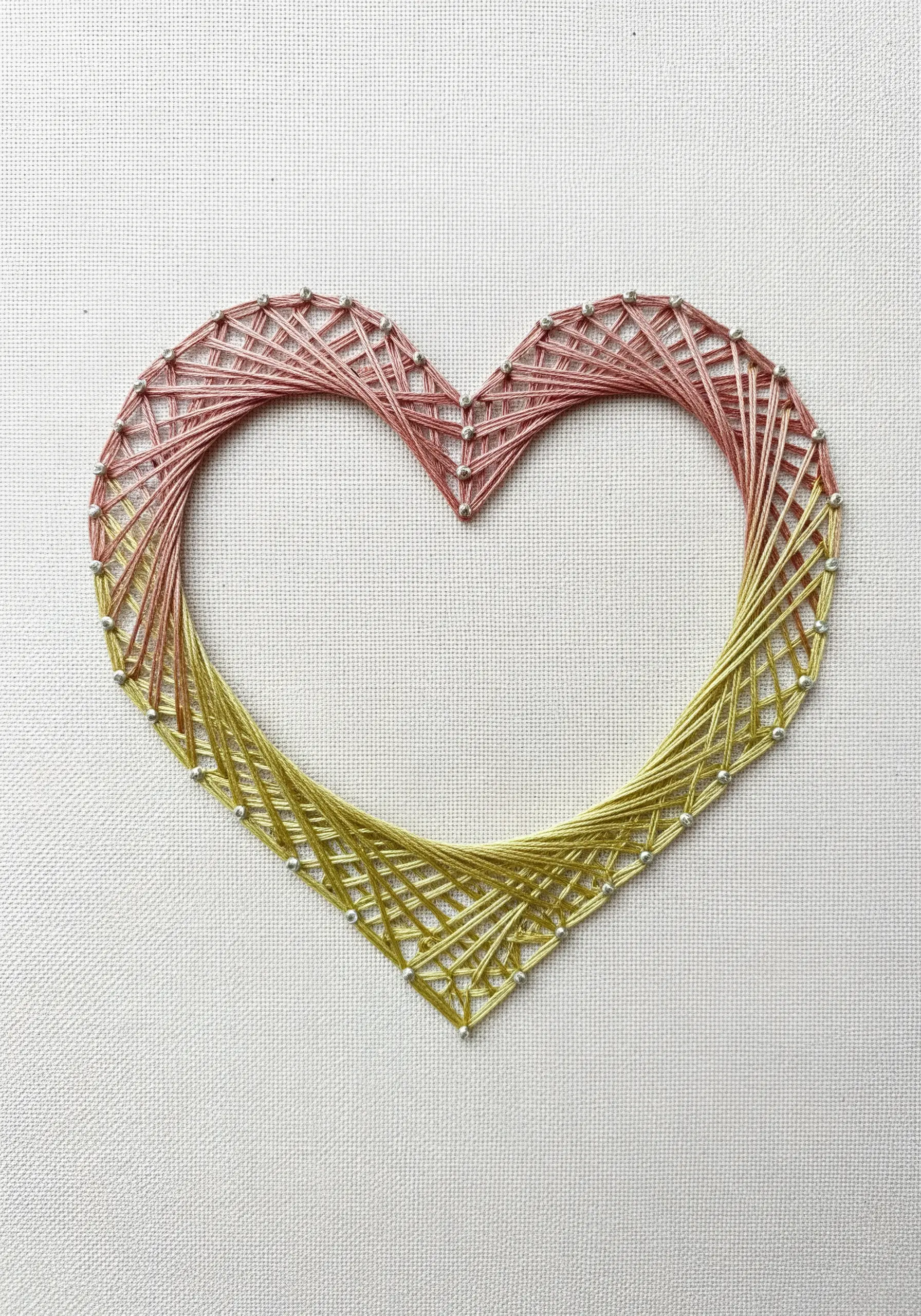 A string art heart outline in two colors, pink and gold, with a completely empty center.