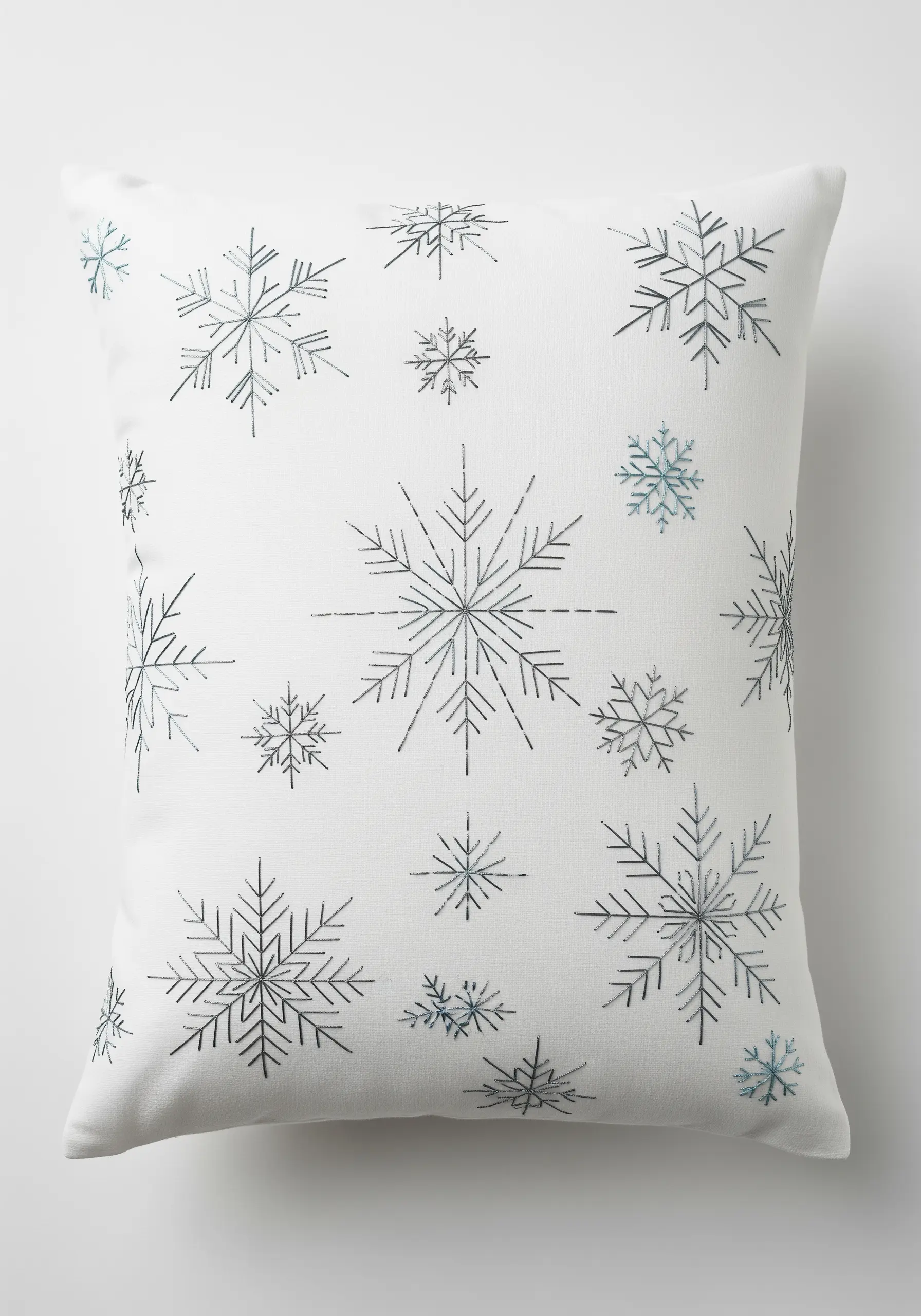 Minimalist silver and blue embroidered snowflakes scattered on a white pillow.