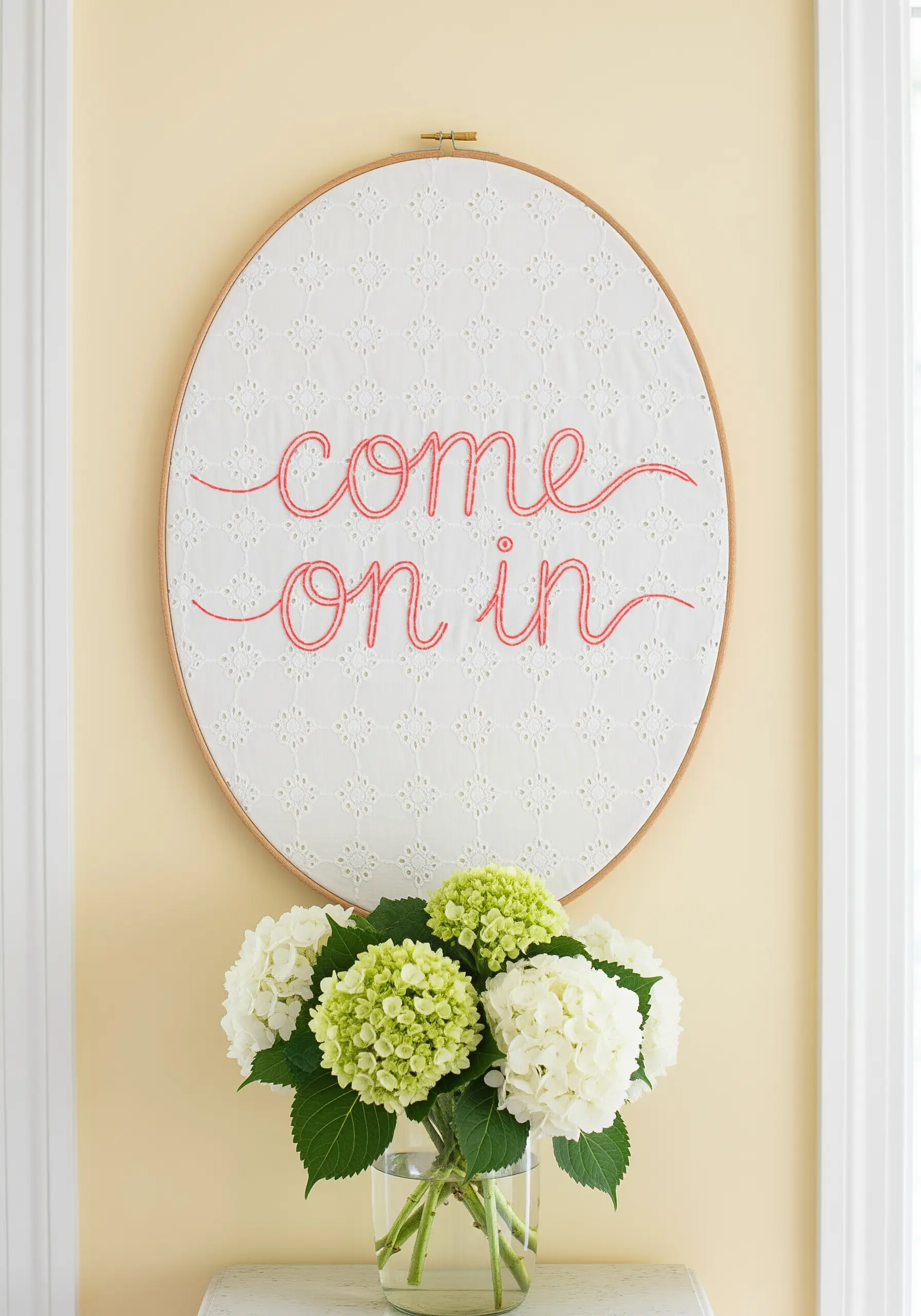 'Come on in' stitched in bright coral thread on a white eyelet lace fabric.