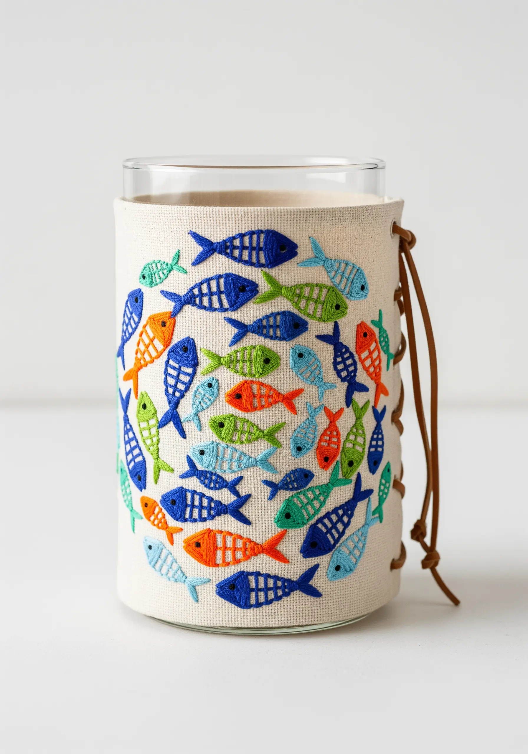 A canvas sleeve embroidered with a pattern of colorful, stylized fish, wrapped around a glass.