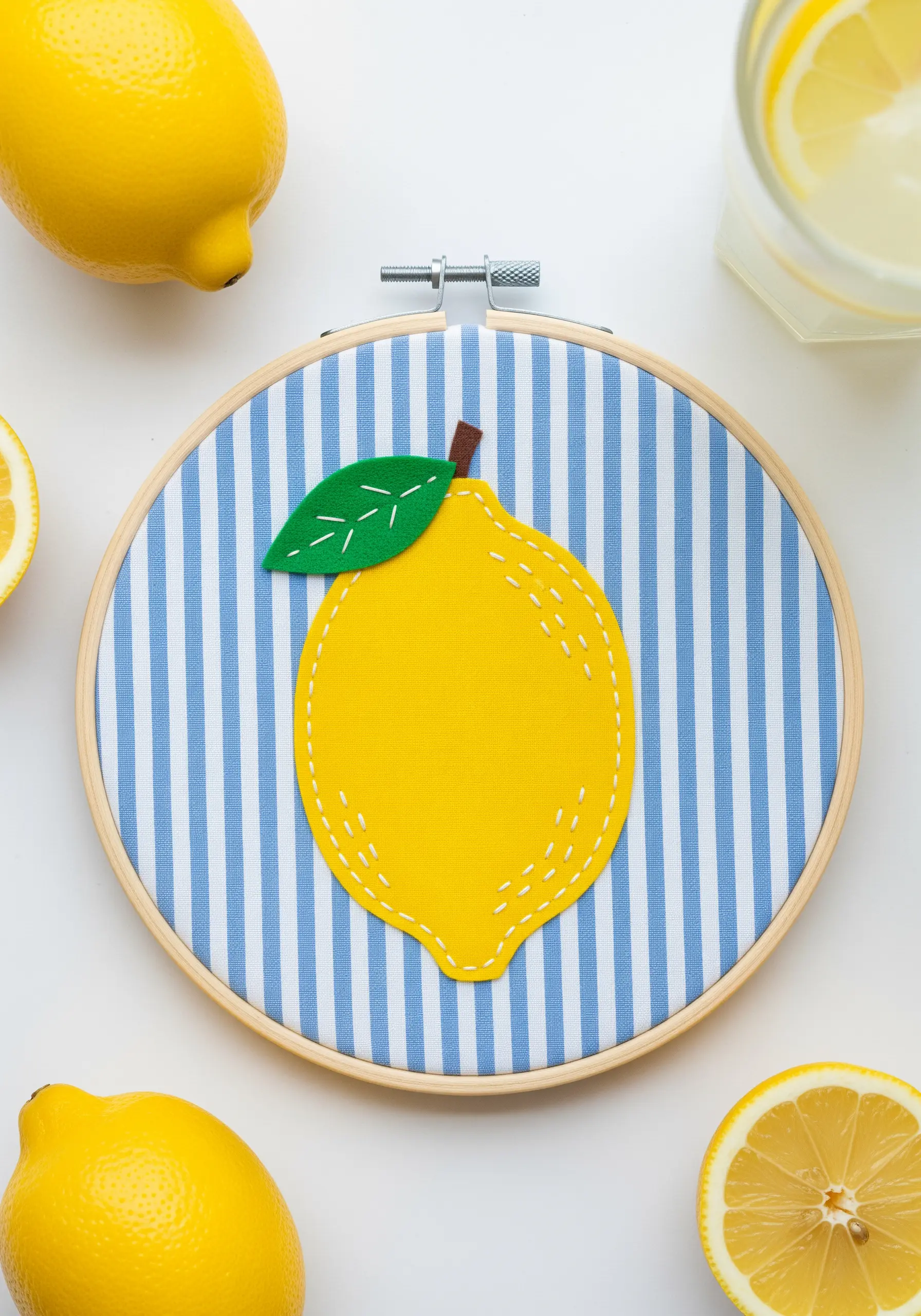 A yellow fabric lemon appliqué with white running stitch on a blue and white striped background.