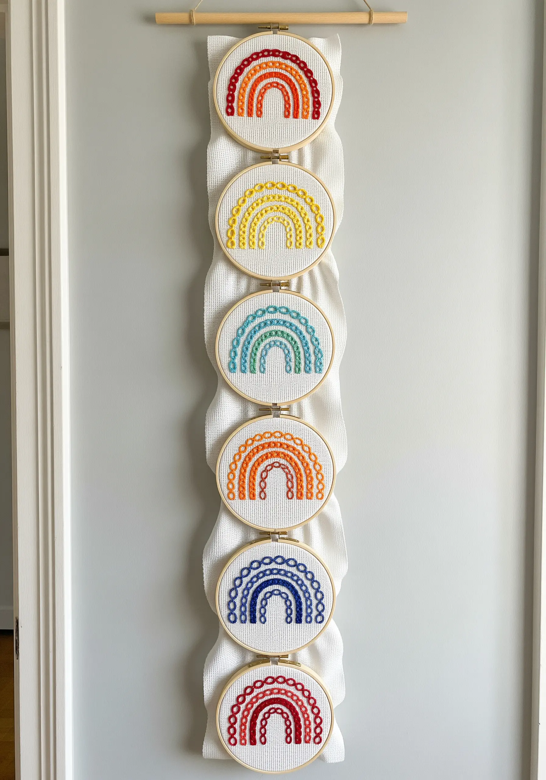 A vertical wall hanging made of multiple hoops, each embroidered with a different colored rainbow.