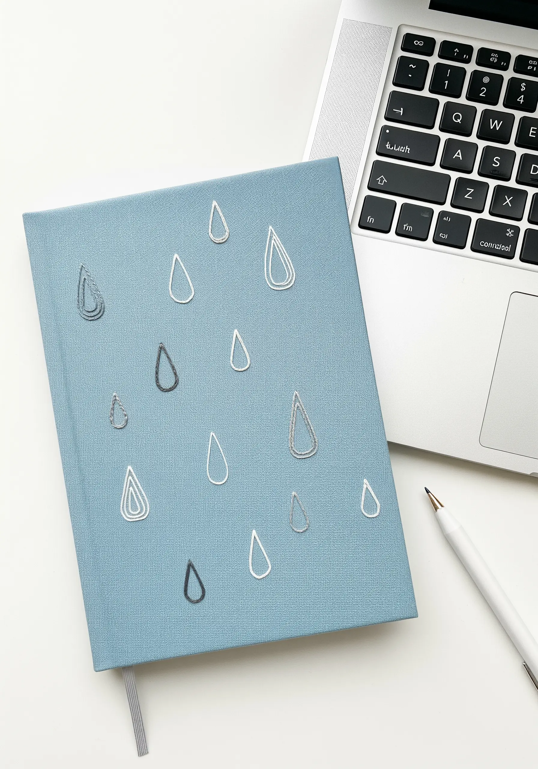 Minimalist raindrop outlines embroidered in silver and grey thread on a notebook.