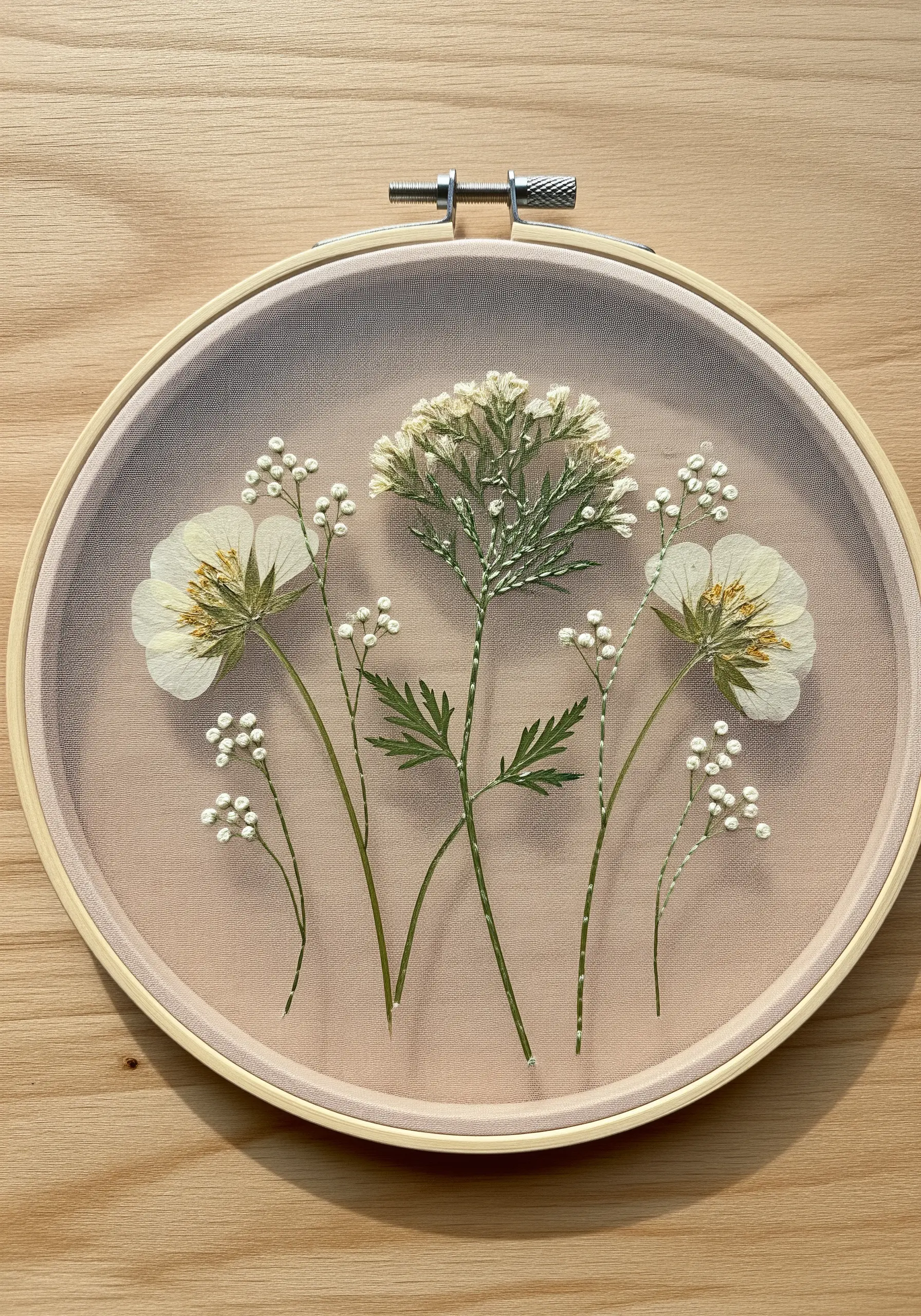 Pressed white and green flowers secured between two layers of sheer tulle in an embroidery hoop.