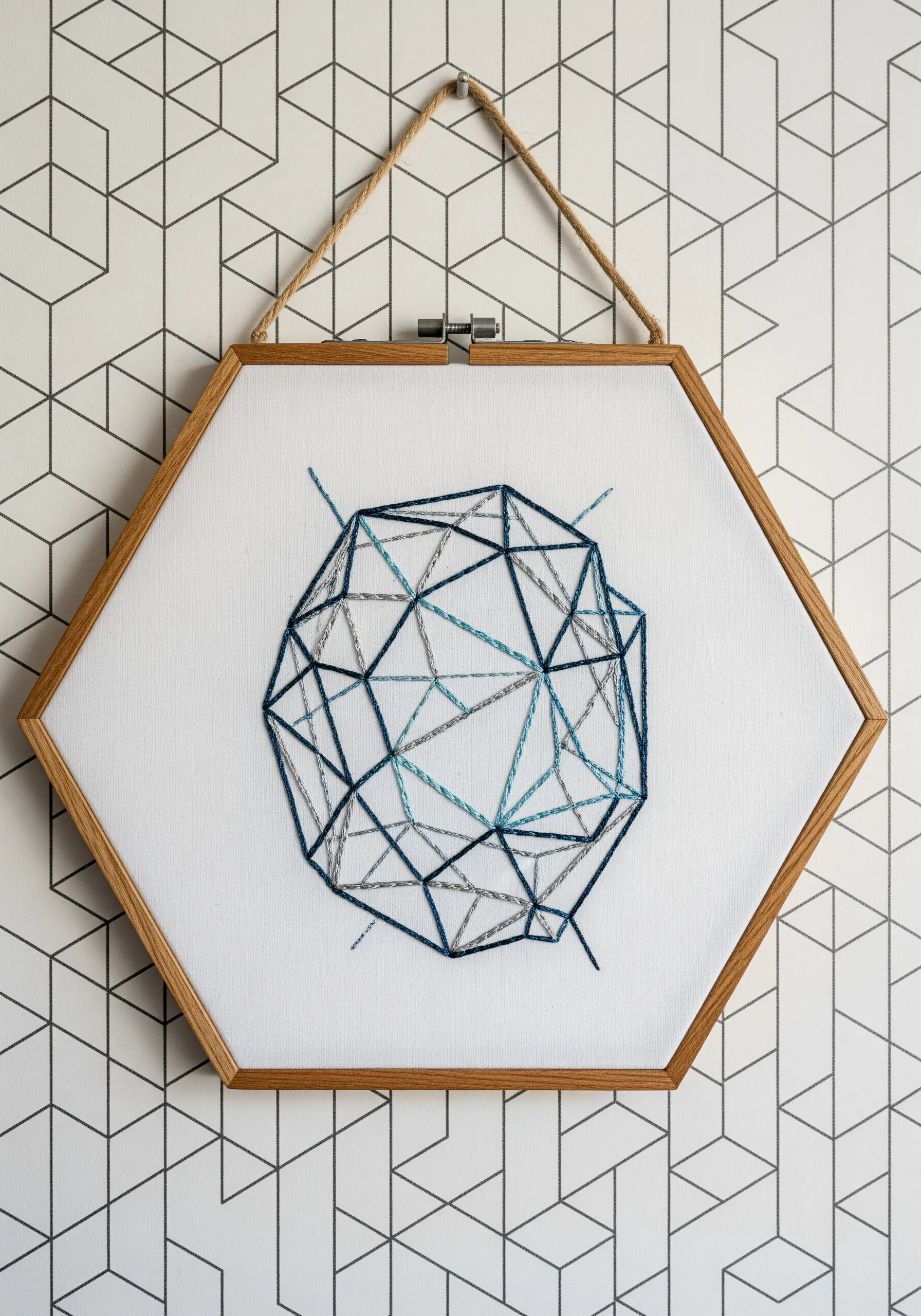 A geometric, prism-like shape embroidered in shades of blue on white fabric in a hexagonal hoop.