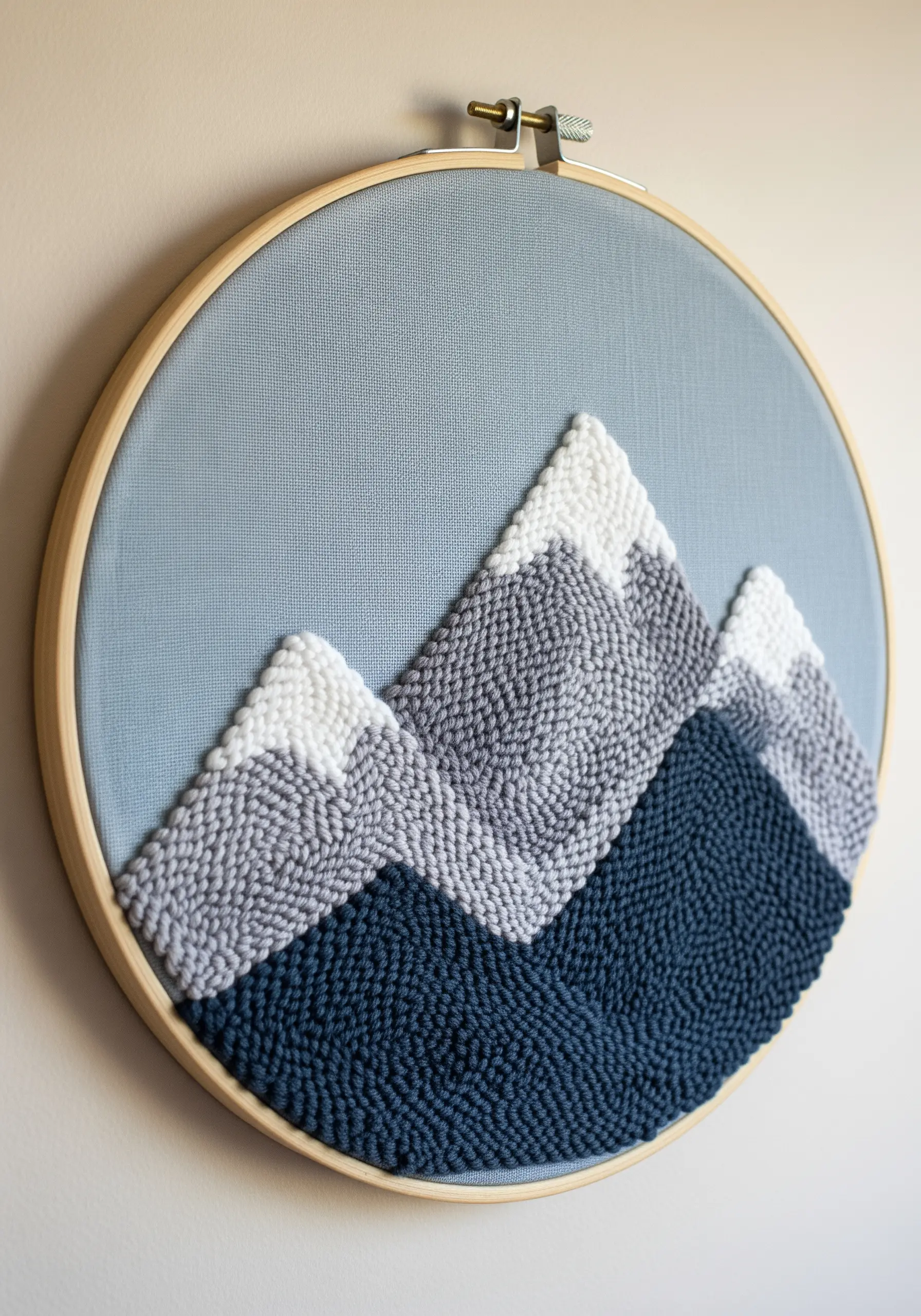 Punch needle art in a hoop depicting a mountain range in shades of blue, grey, and white.