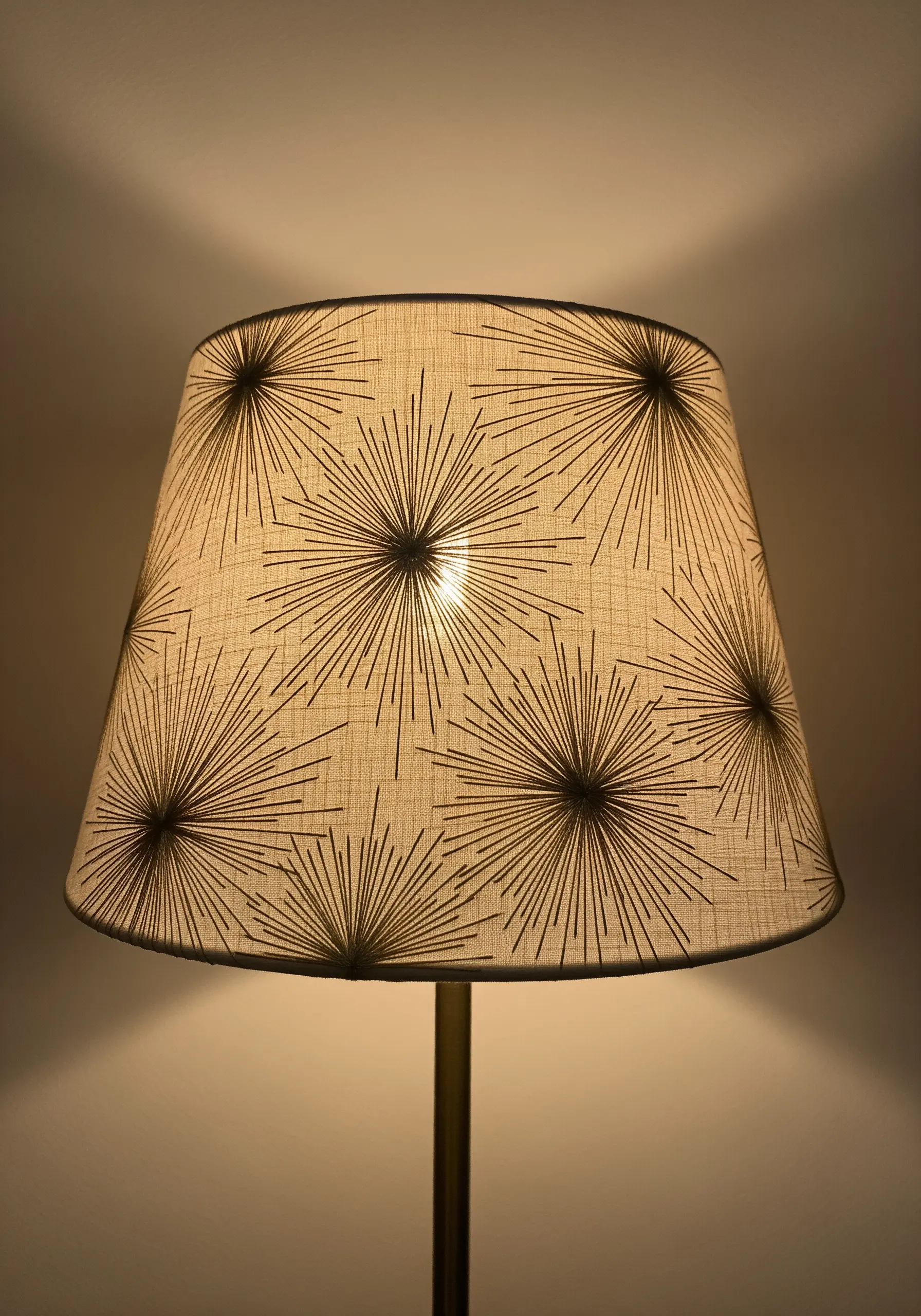 A fabric lampshade decorated with embroidered starburst patterns in black thread.