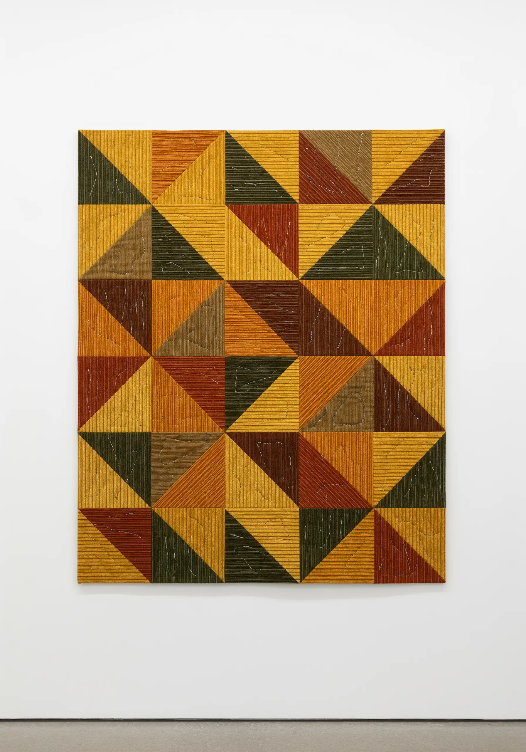 A square quilted wall hanging with a geometric pattern of triangles in earthy tones.