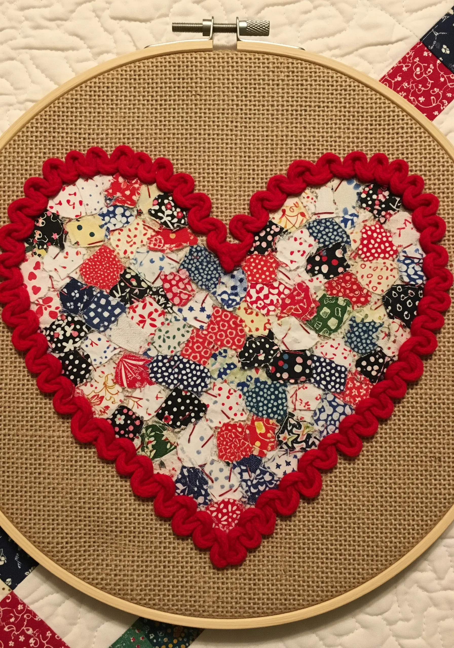 A heart-shaped collage made of tiny, colorful fabric scraps, framed with a red textured stitch.